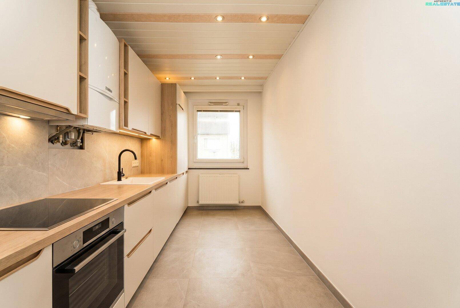 Moderne Küche mit weißen Schränken, Holz-Arbeitsplatten und Induktionskochfeld.