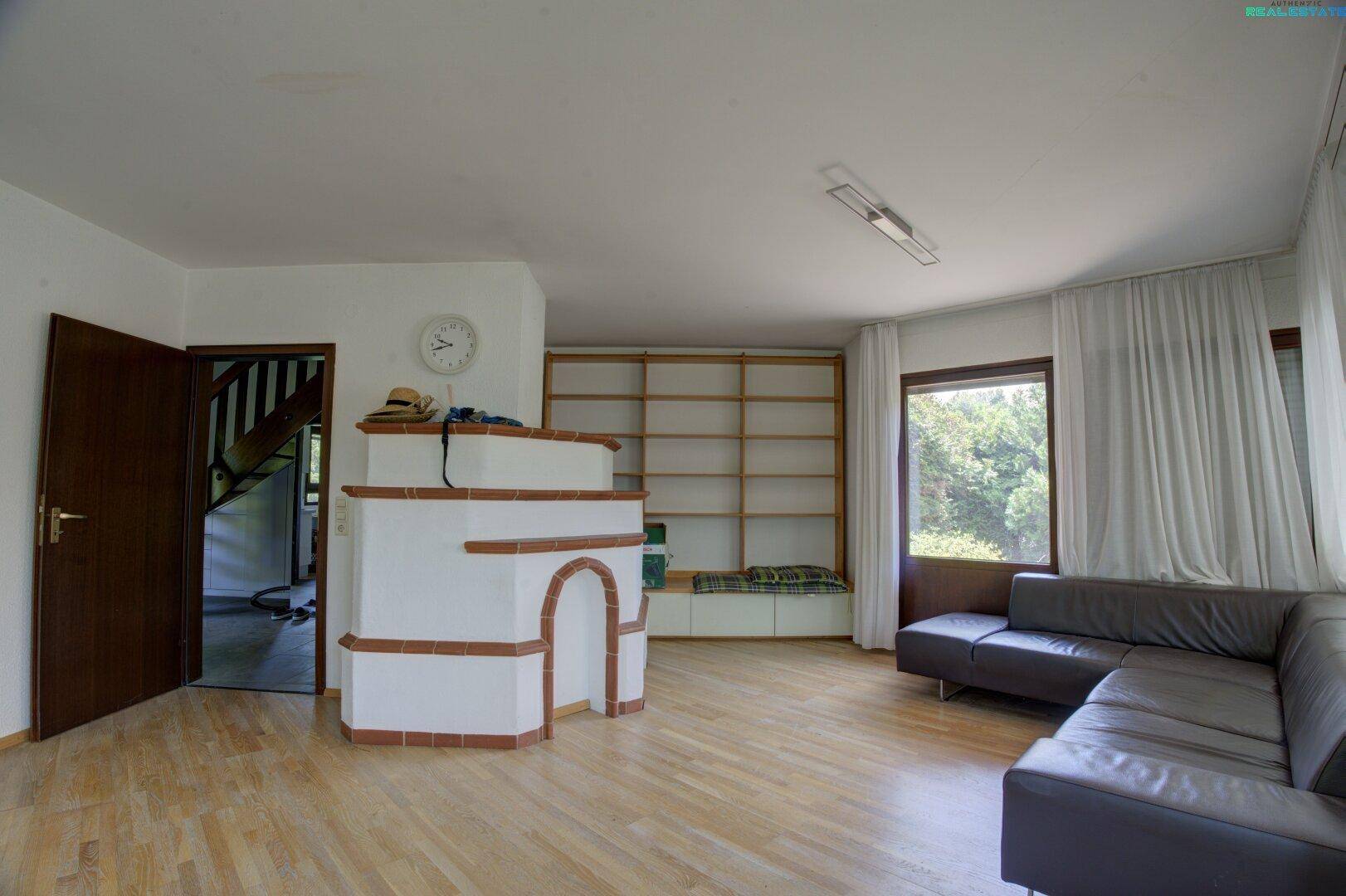 Geräumiges Wohnzimmer mit traditionellem Kachelofen, Holzparkett und Blick in den Garten.