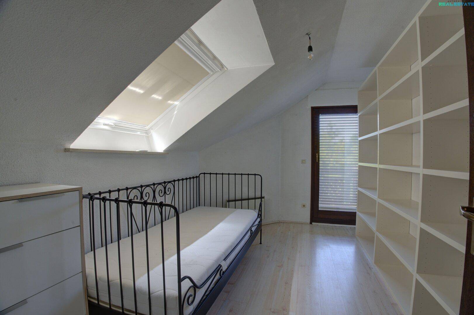 Gemütliches Schlafzimmer im Dachgeschoss mit schräger Decke, Dachfenster und integriertem Regal.