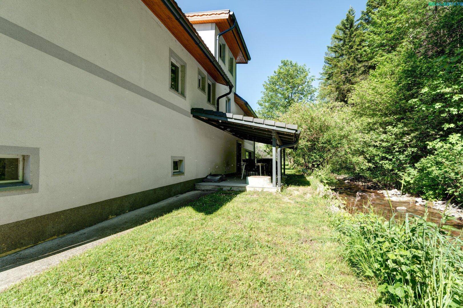 Seitenansicht des Hauses mit angrenzendem Bach und viel Grün.