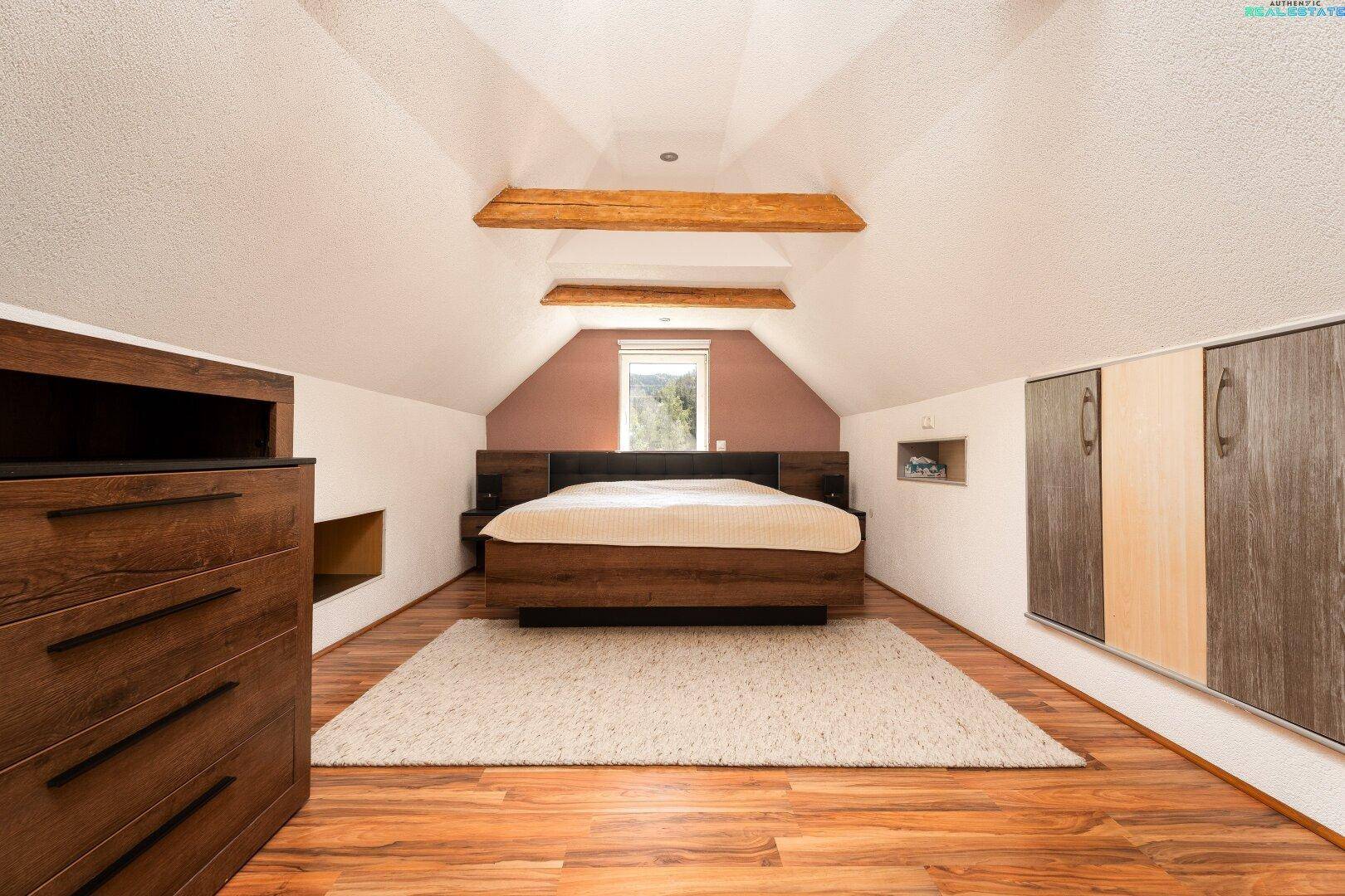 Schlafzimmer im Dachgeschoss mit Holzbalken und Holzboden.