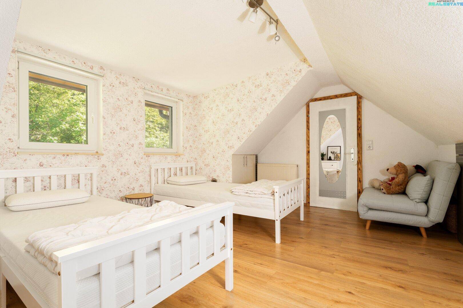 Kinderzimmer im Dachgeschoss mit zwei Betten und floraler Tapete.