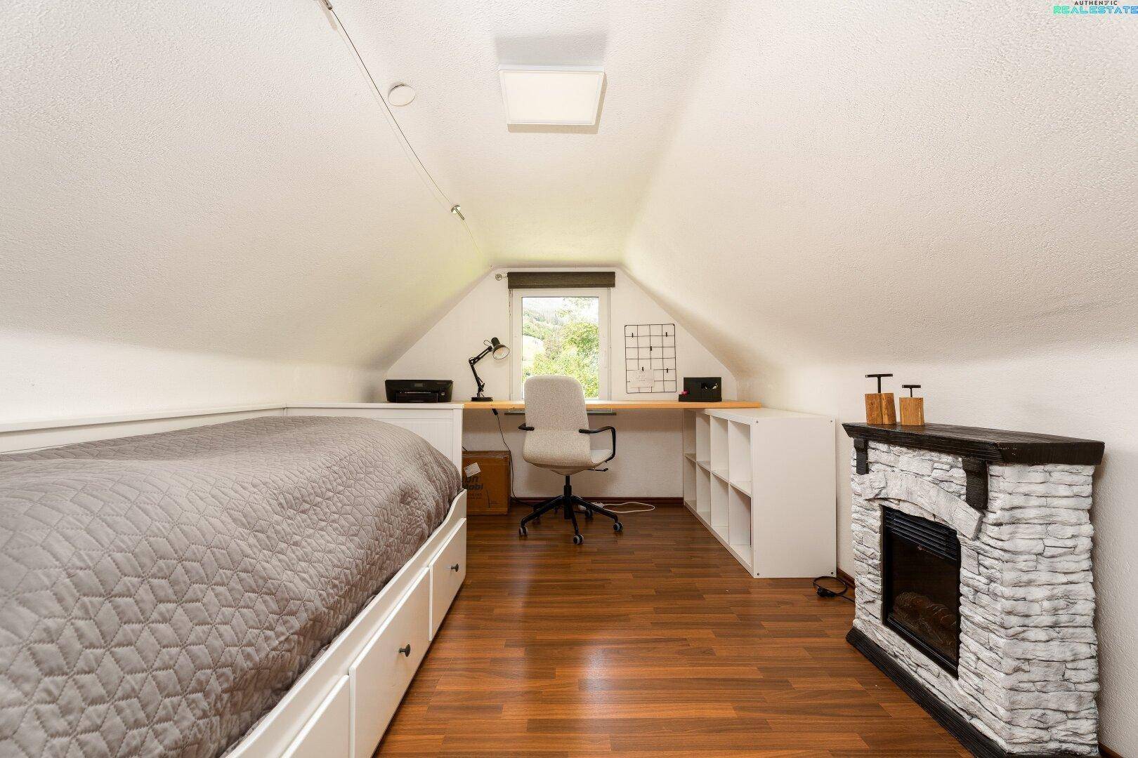 Arbeitszimmer im Dachgeschoss mit Schreibtisch, Bett und Kaminattrappe.
