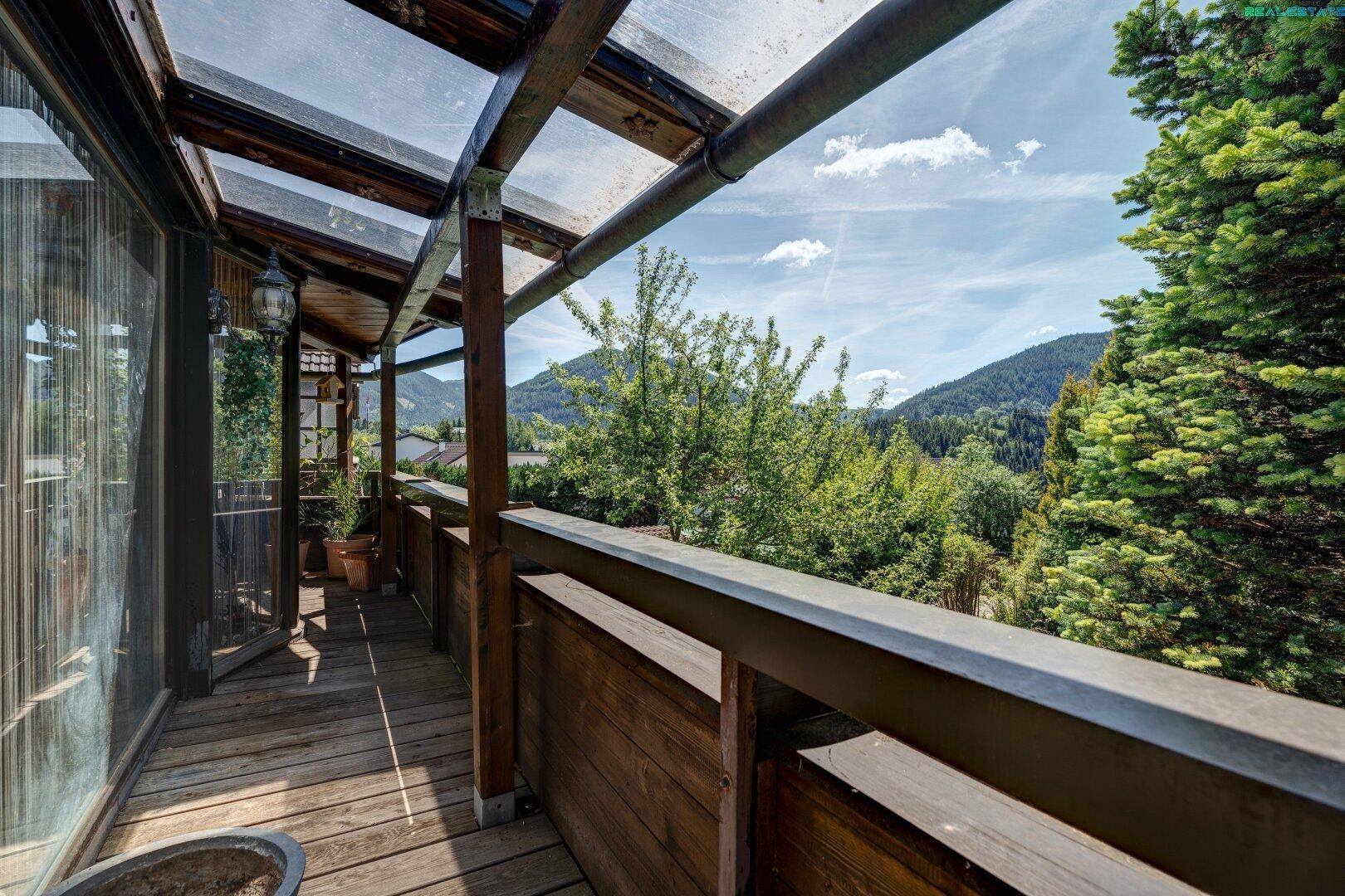Überdachter Holzbalkon mit Bergblick und viel Grün, ideal zum Entspannen im Freien.