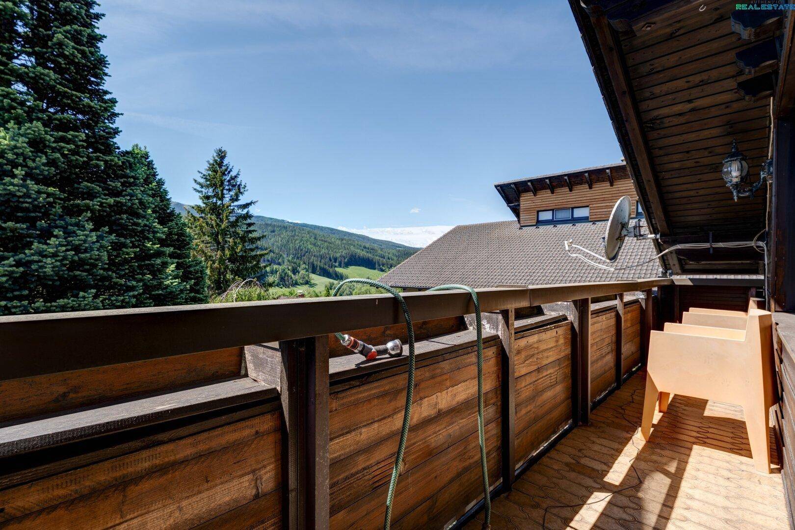 Geräumiger Holzbalkon mit weitem Blick auf die Berge und die grüne Landschaft.