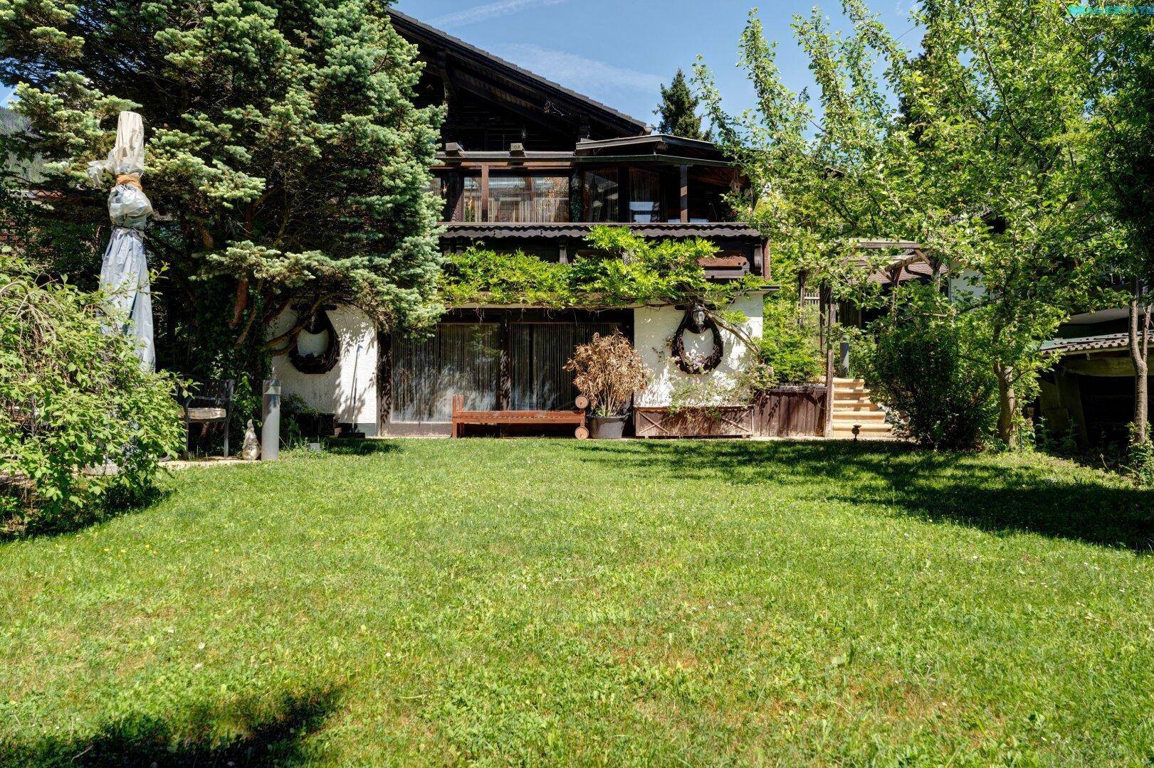 Großzügiger Garten mit Rasenfläche, alten Bäumen und einer gemütlichen Sitzbank vor dem Haus.