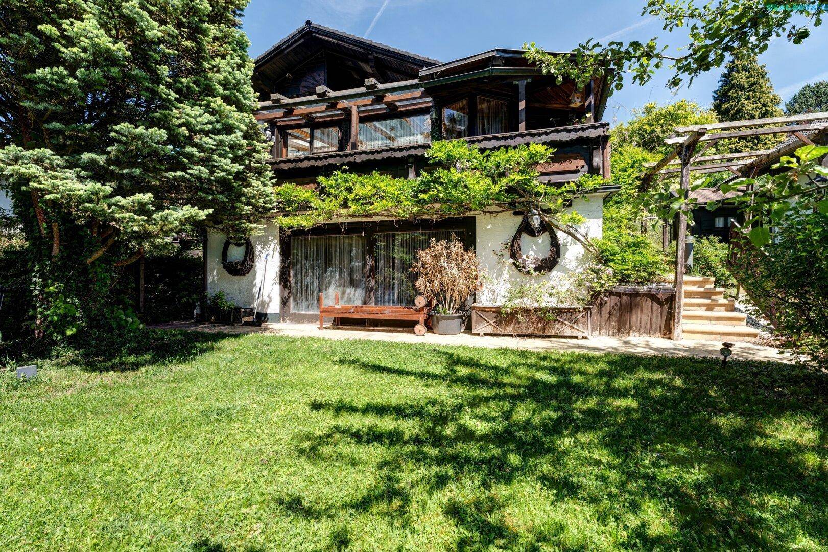 Großzügiger Garten mit Rasenfläche, alten Bäumen und einer gemütlichen Sitzbank vor dem Haus.
