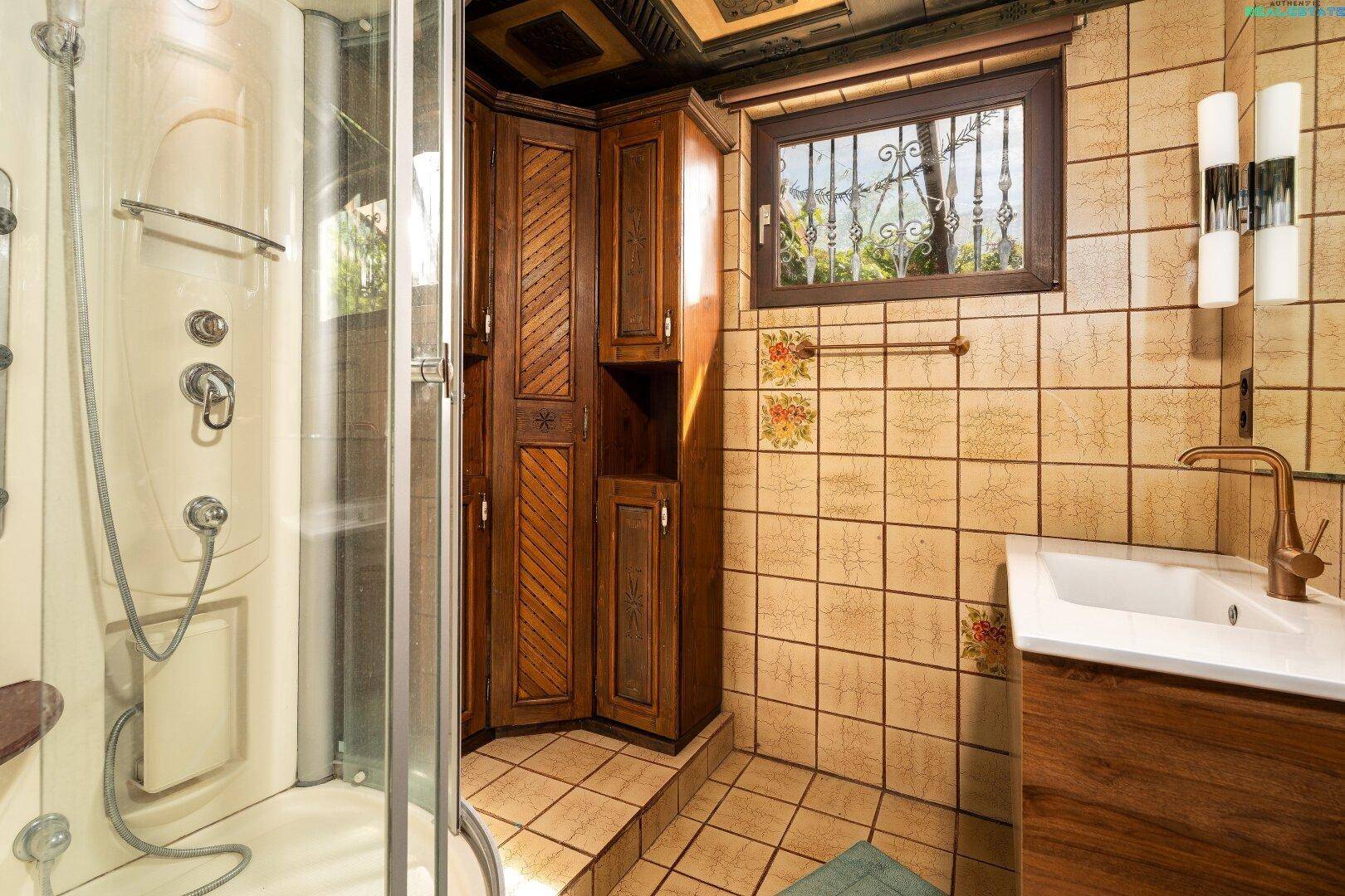 Badezimmer mit Duschkabine, Holzschrank und traditionellen Fliesen.