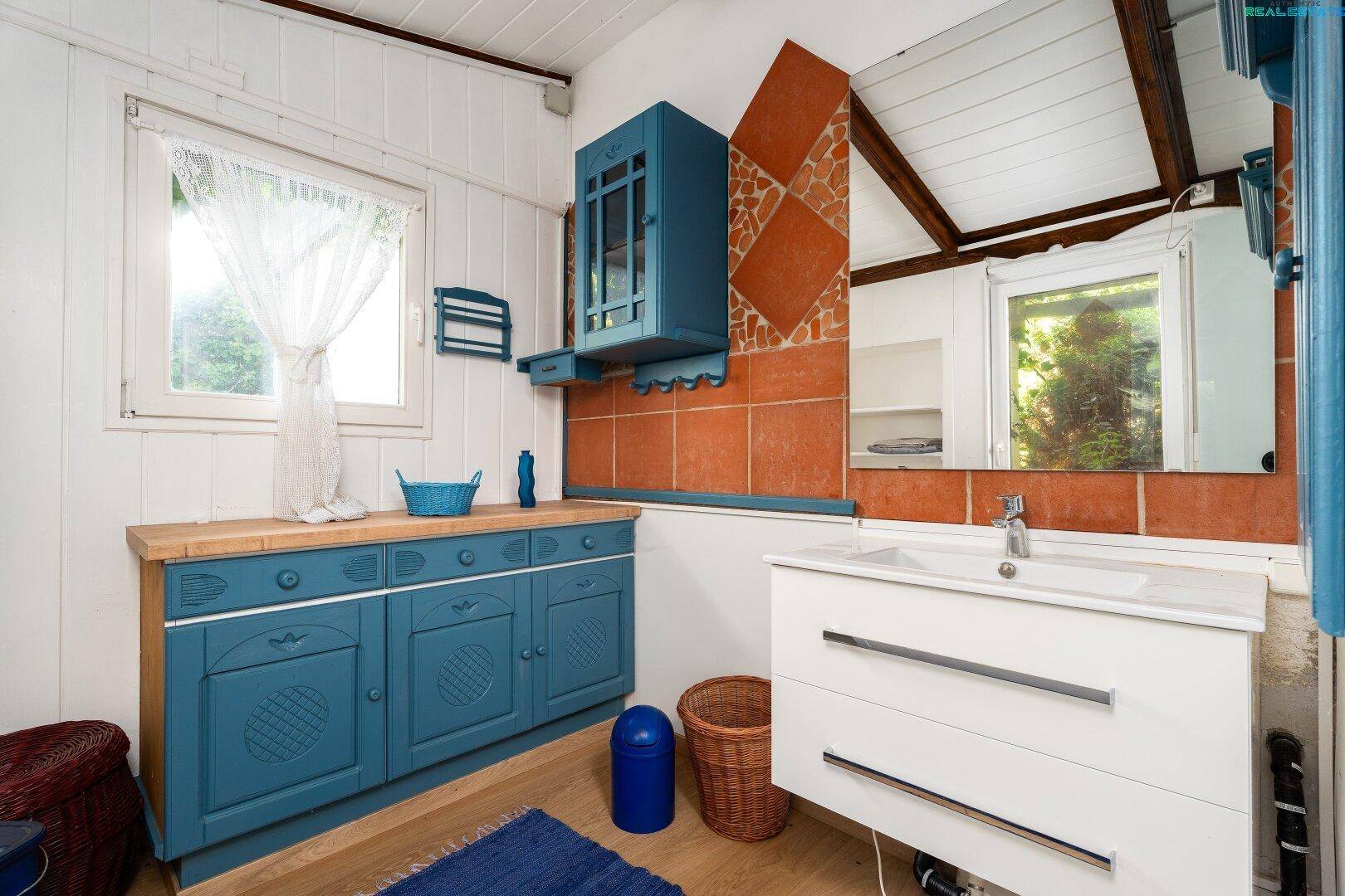 Helles Badezimmer mit blauen Schränken, Holzwaschtisch und Fenster.