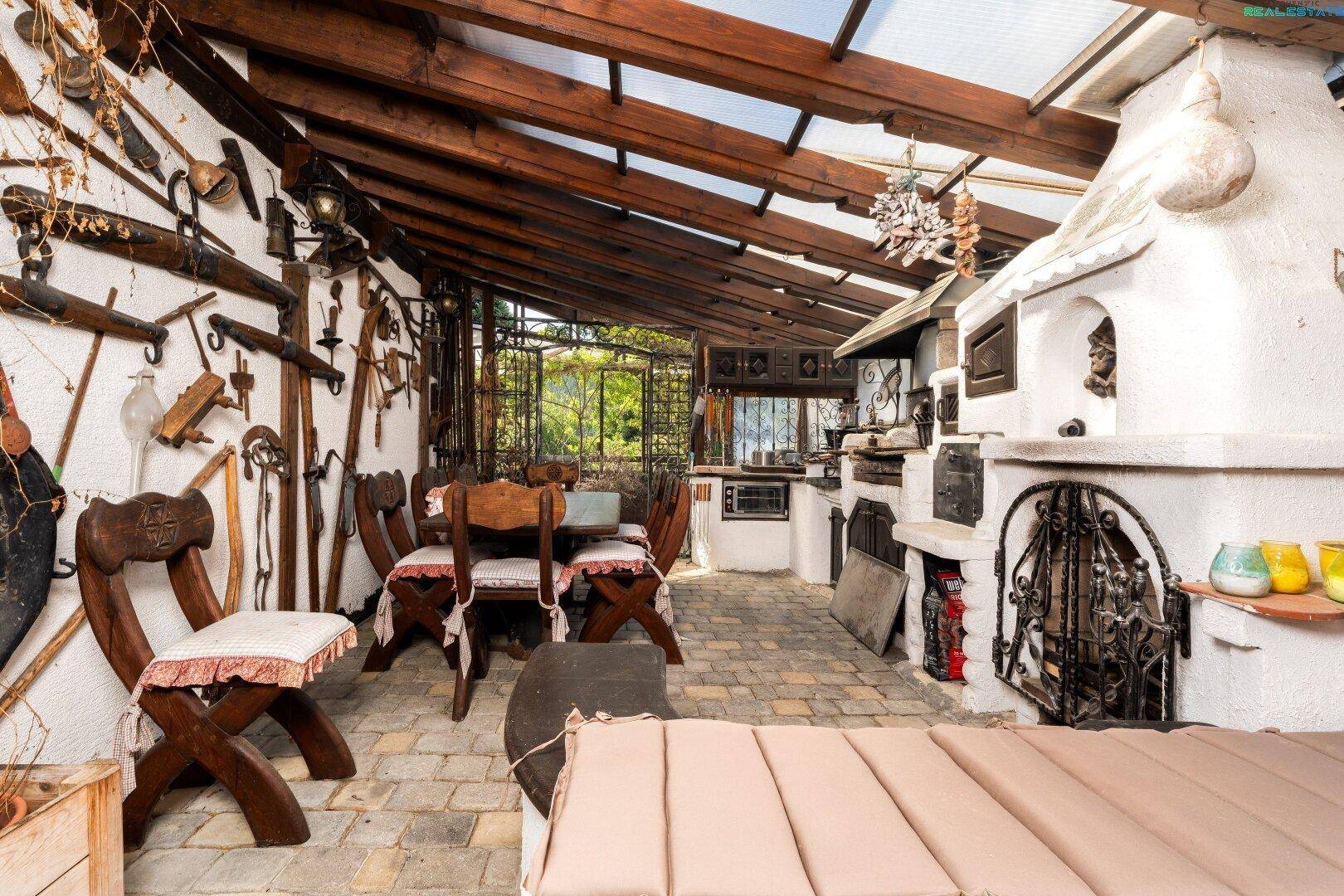 Überdachter Essbereich mit rustikalen Holzmöbeln und einem traditionellen Steinofen.