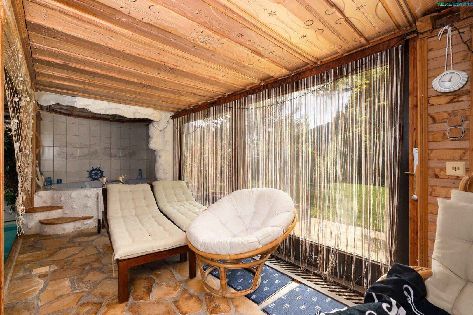 Entspannungsbereich am Pool mit bequemen Rattanmöbeln und Blick in den Garten.