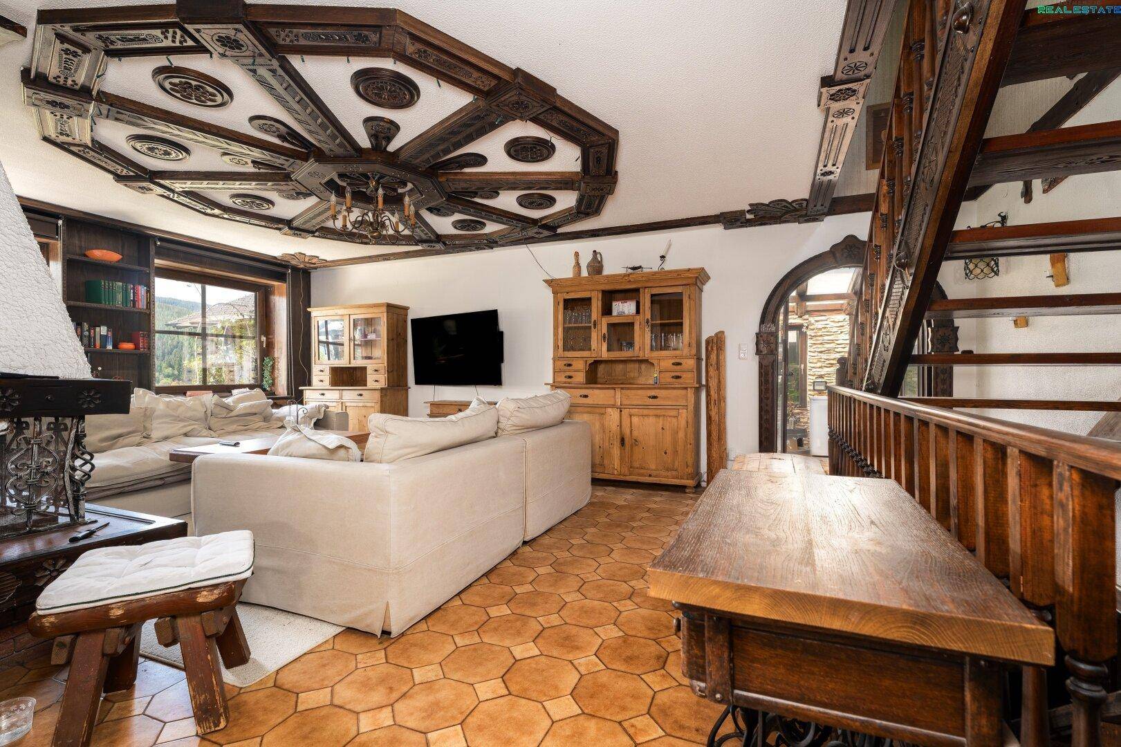 Gemütlicher Wohnbereich mit traditionellen Holzmöbeln, geschnitzter Decke und Treppenzugang.