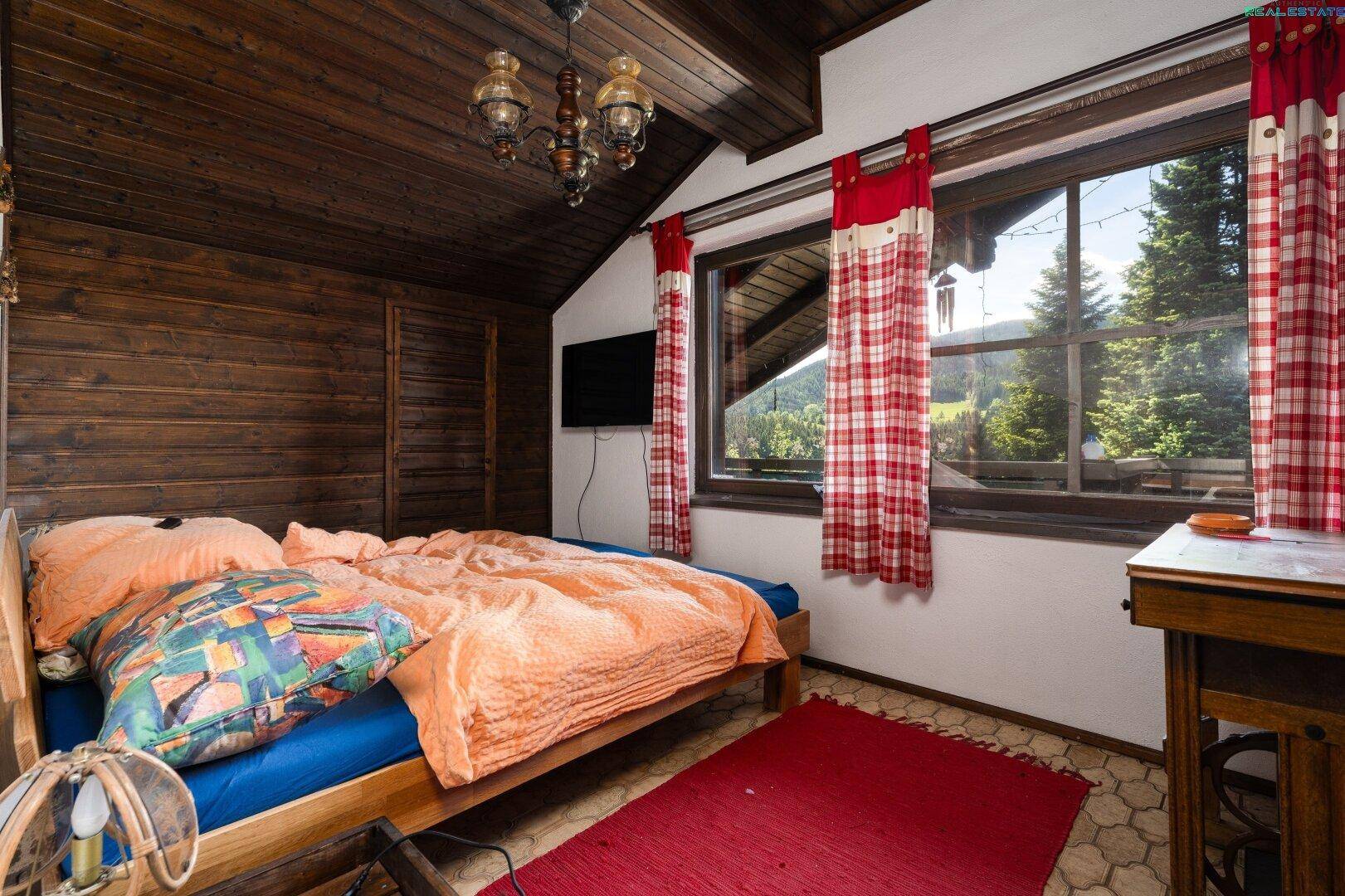 Schlafzimmer mit Holzwänden, Dachschräge und Bergblick durch große Fenster.