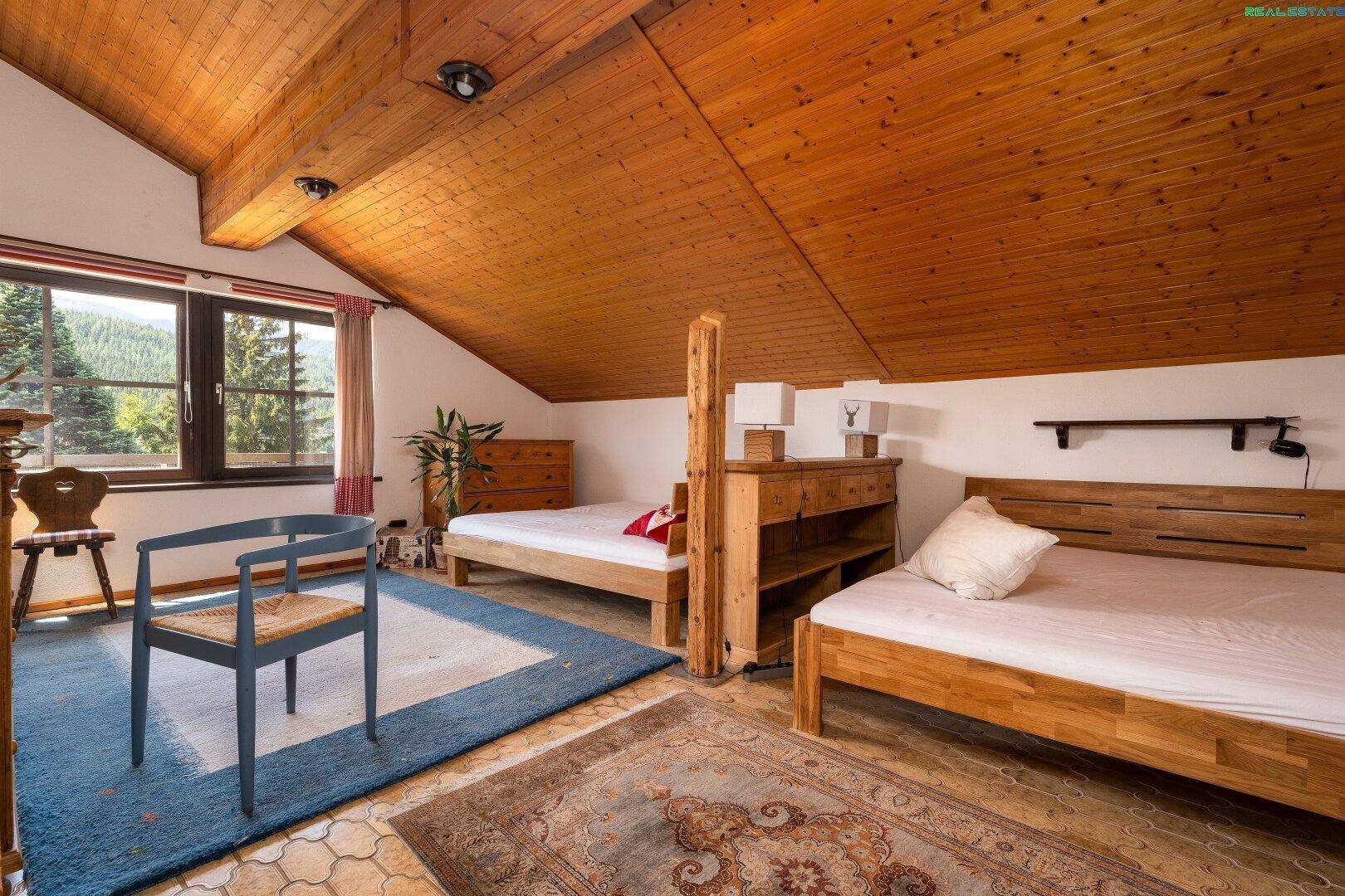 Geräumiges Schlafzimmer im Dachgeschoss mit Holzbalken, zwei Betten und Bergblick.