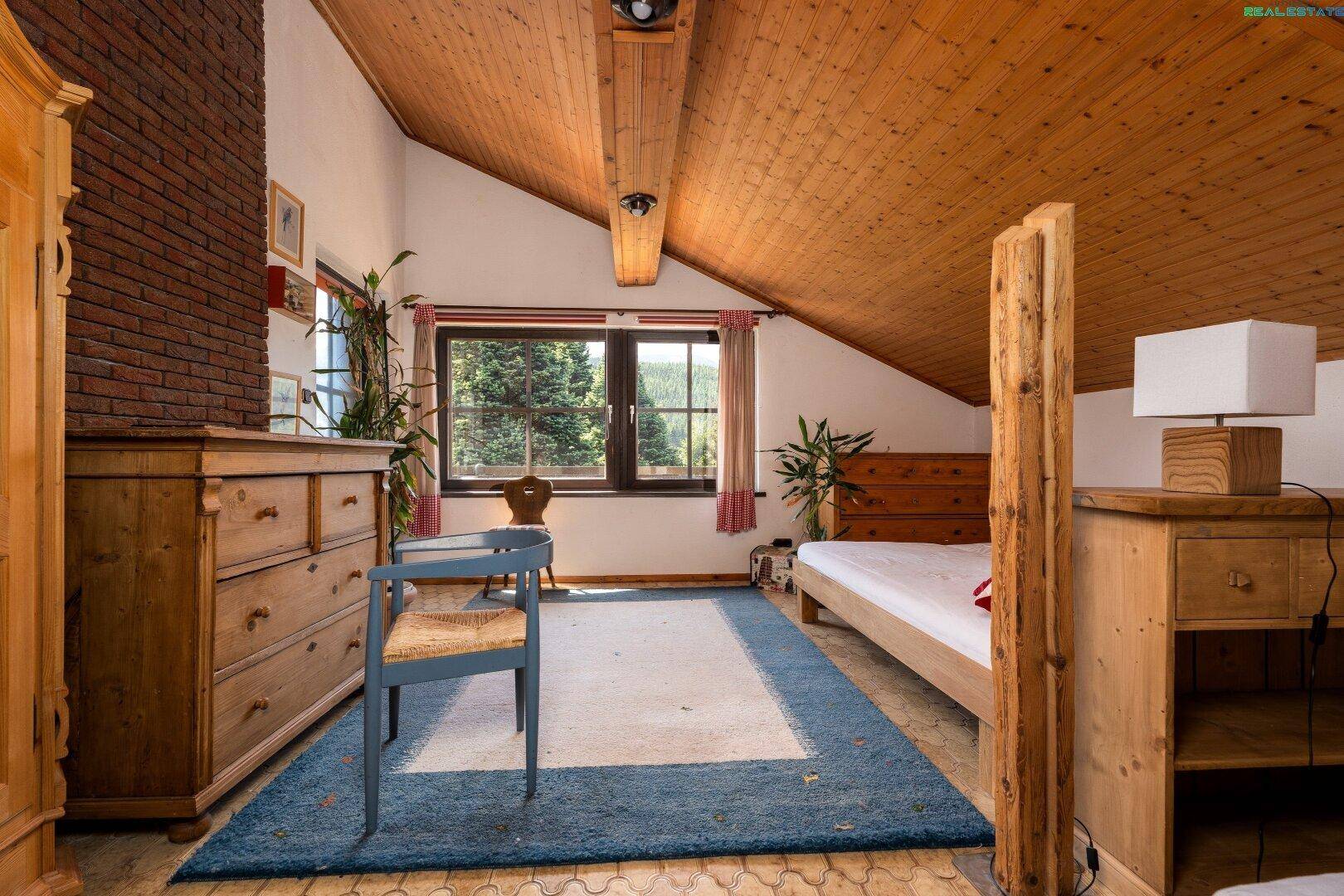 Helles Schlafzimmer im Dachgeschoss mit Holzbalken, großem Fenster und Bergblick.