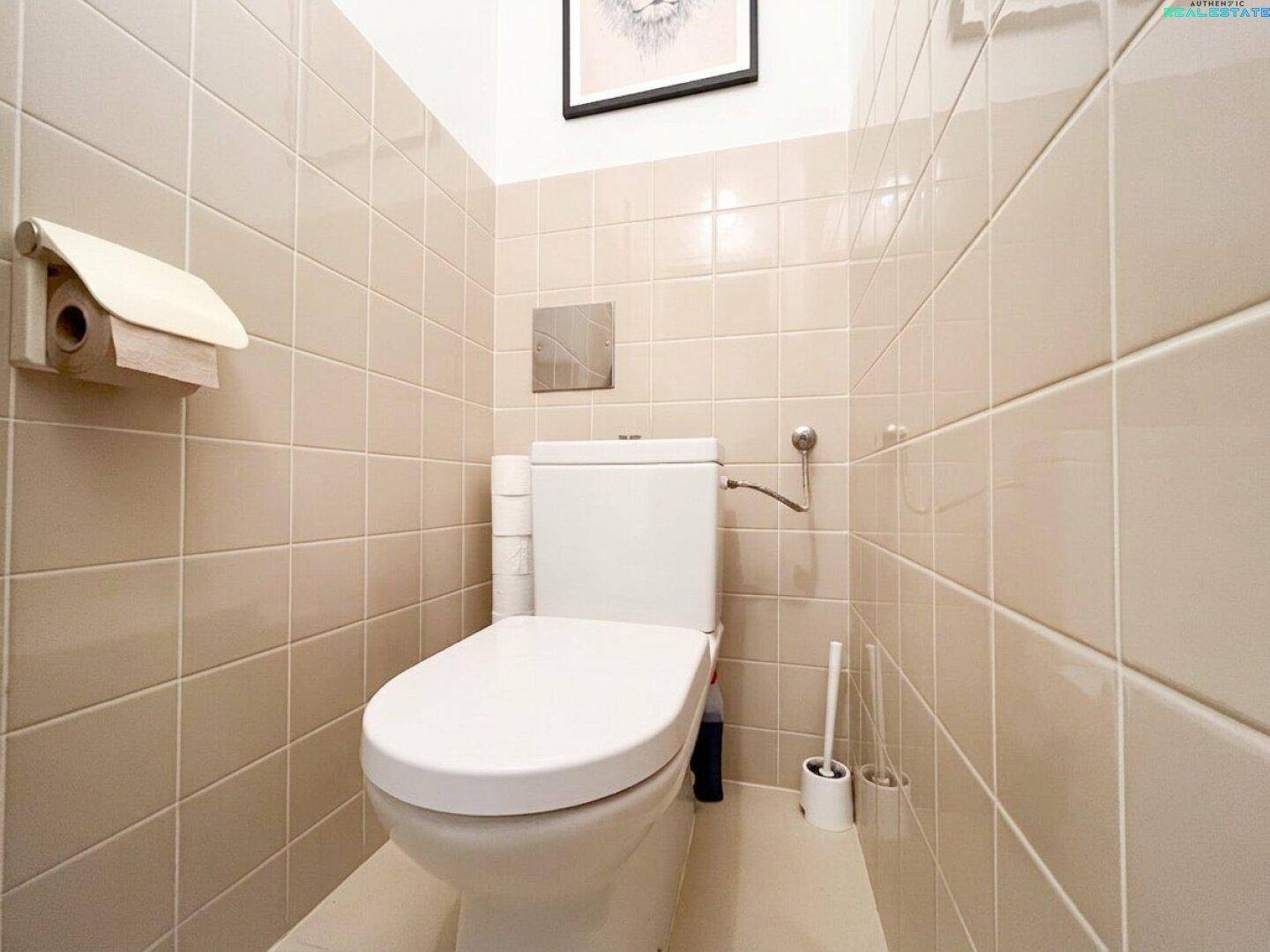 Kleines WC mit beigefarbenen Wand- und Bodenfliesen und wandhängender Toilette.