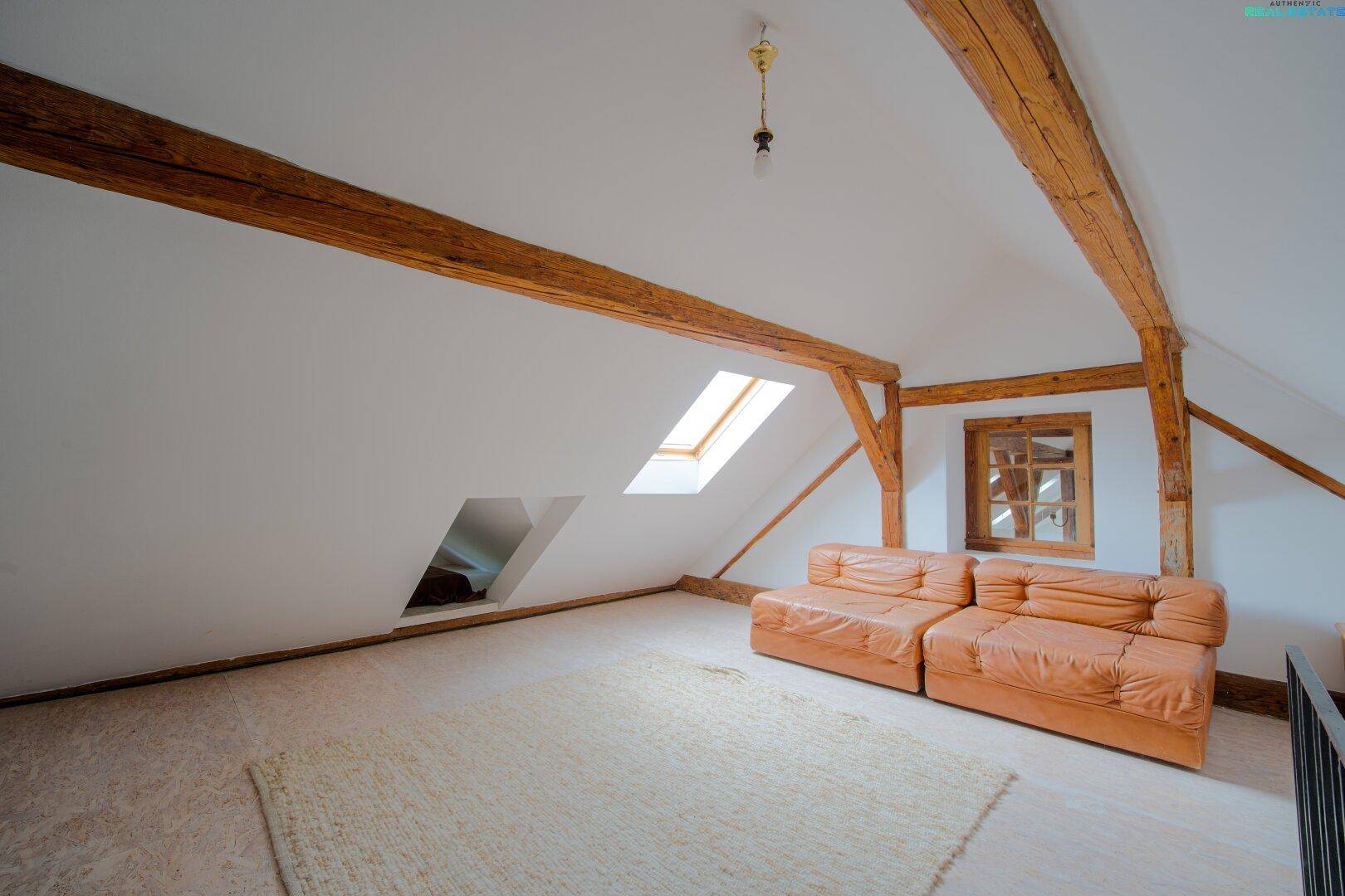 Helles Dachzimmer mit sichtbaren Holzbalken, Dachfenstern und bequemen Ledersofas.