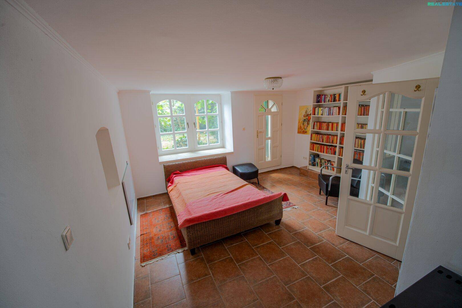 Schlafzimmer mit Terrakottafliesen, großen Fenstern und einem Bücherregal.