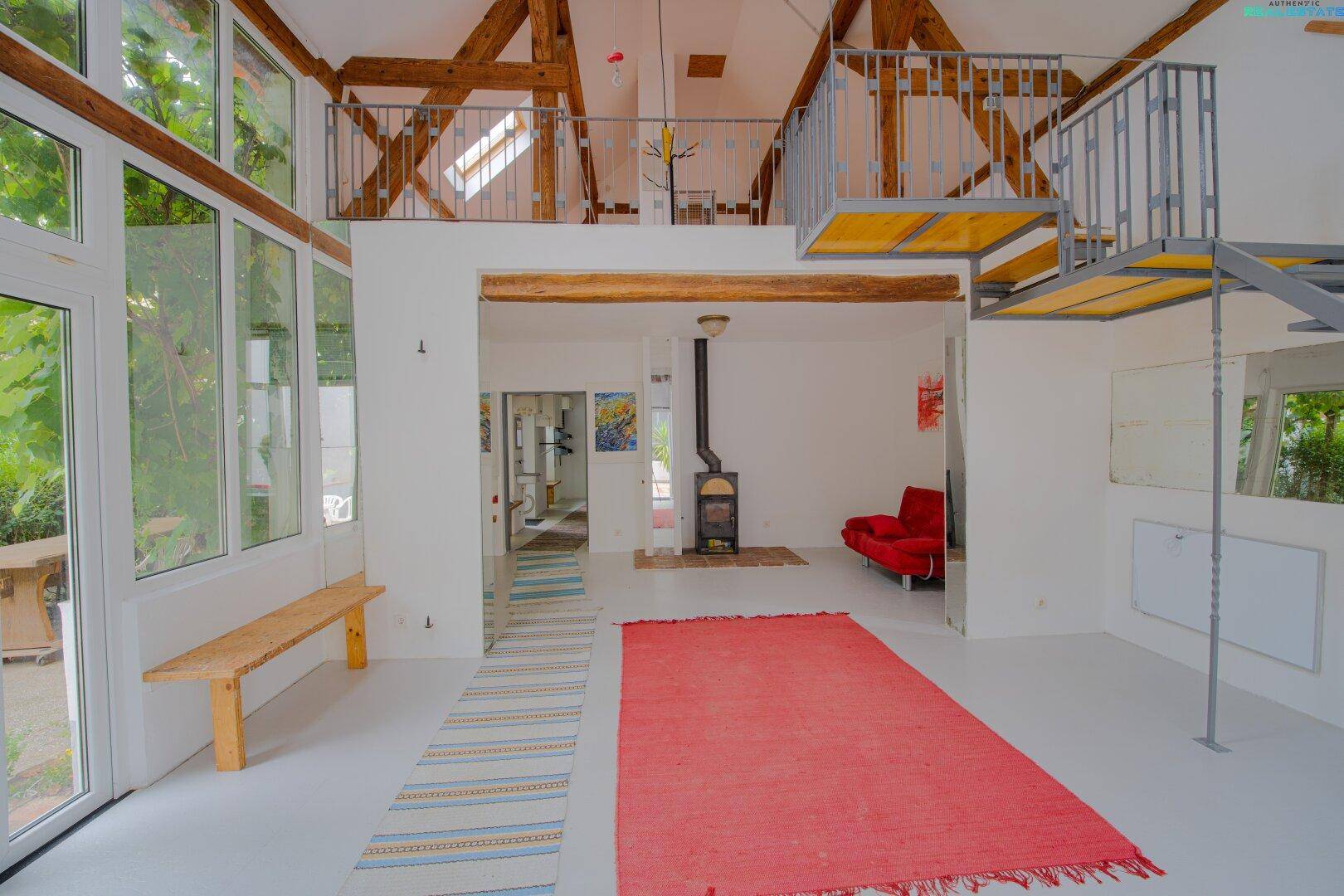 Offener Wohnbereich mit Kaminofen, hohen Decken, Galerie und großen Fenstern.