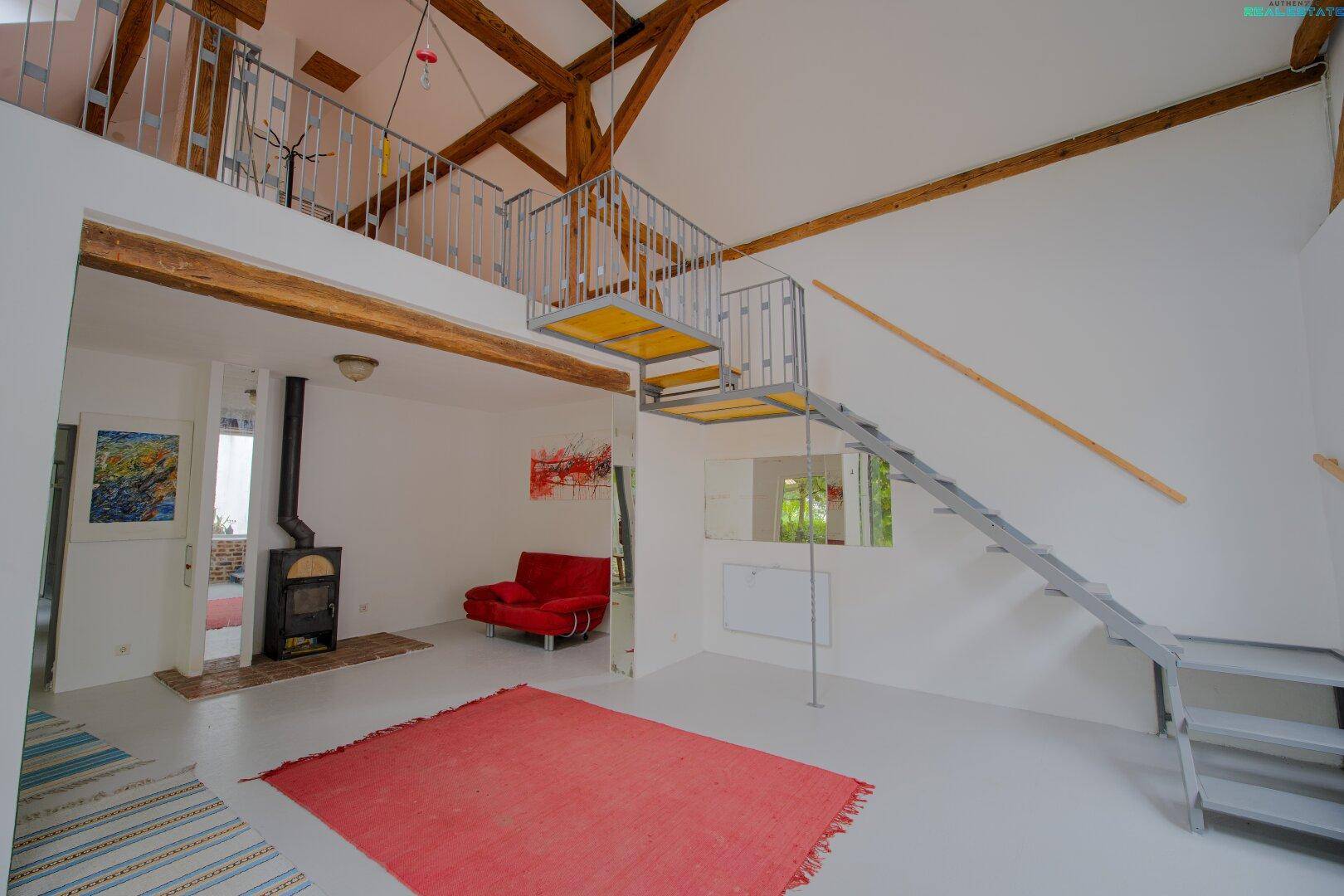 Heller Wohnbereich mit Galerie, hohen Decken, Kaminofen und moderner Treppe.