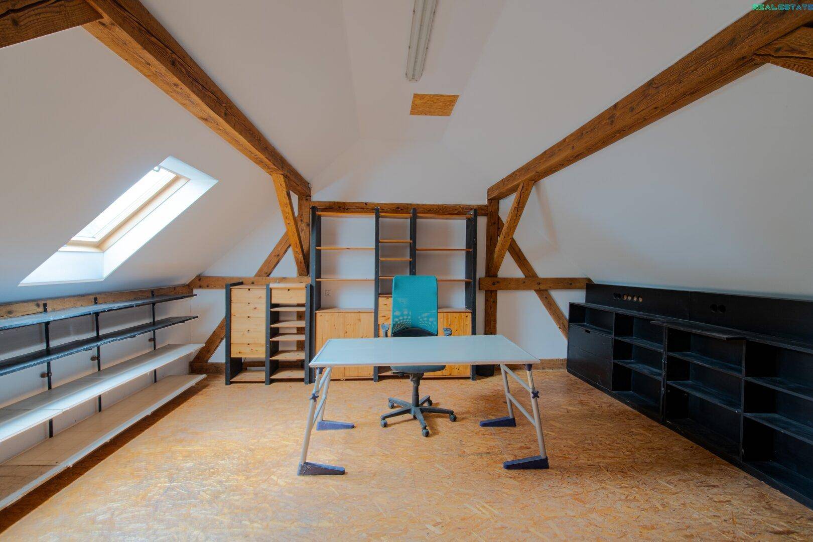 Geräumiges Dachzimmer als Büro mit Regalen, Schreibtisch und Dachfenster.