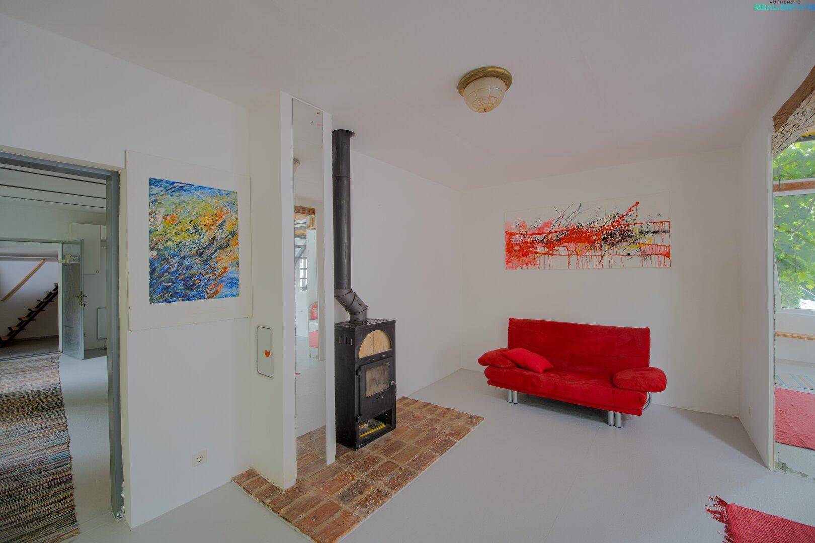 Heller Wohnbereich mit Kaminofen, rotem Sofa und abstrakten Kunstwerken an den Wänden.