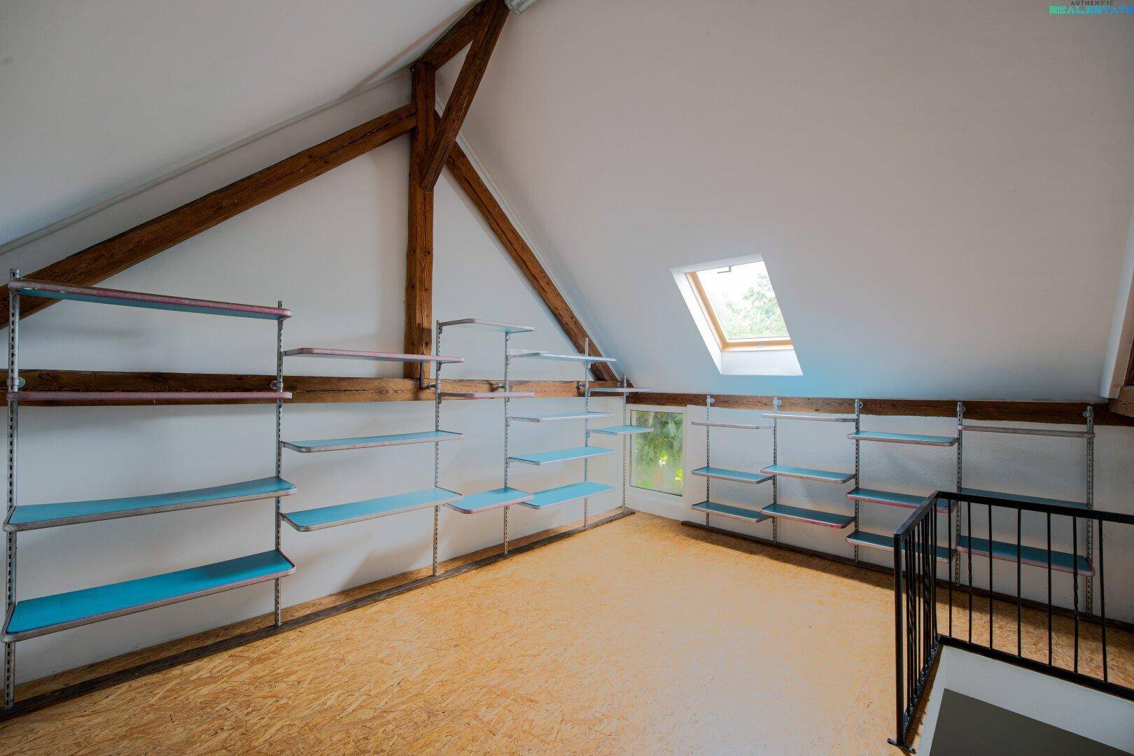 Dachboden mit Regalsystemen, Holzbalken und einem Dachfenster für Tageslicht.