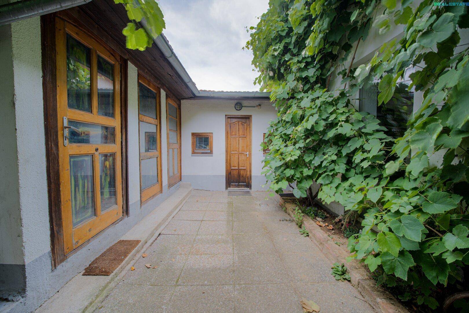 Gepflasterter Außenbereich zwischen Gebäuden mit Holztüren und bewachsenen Wänden.