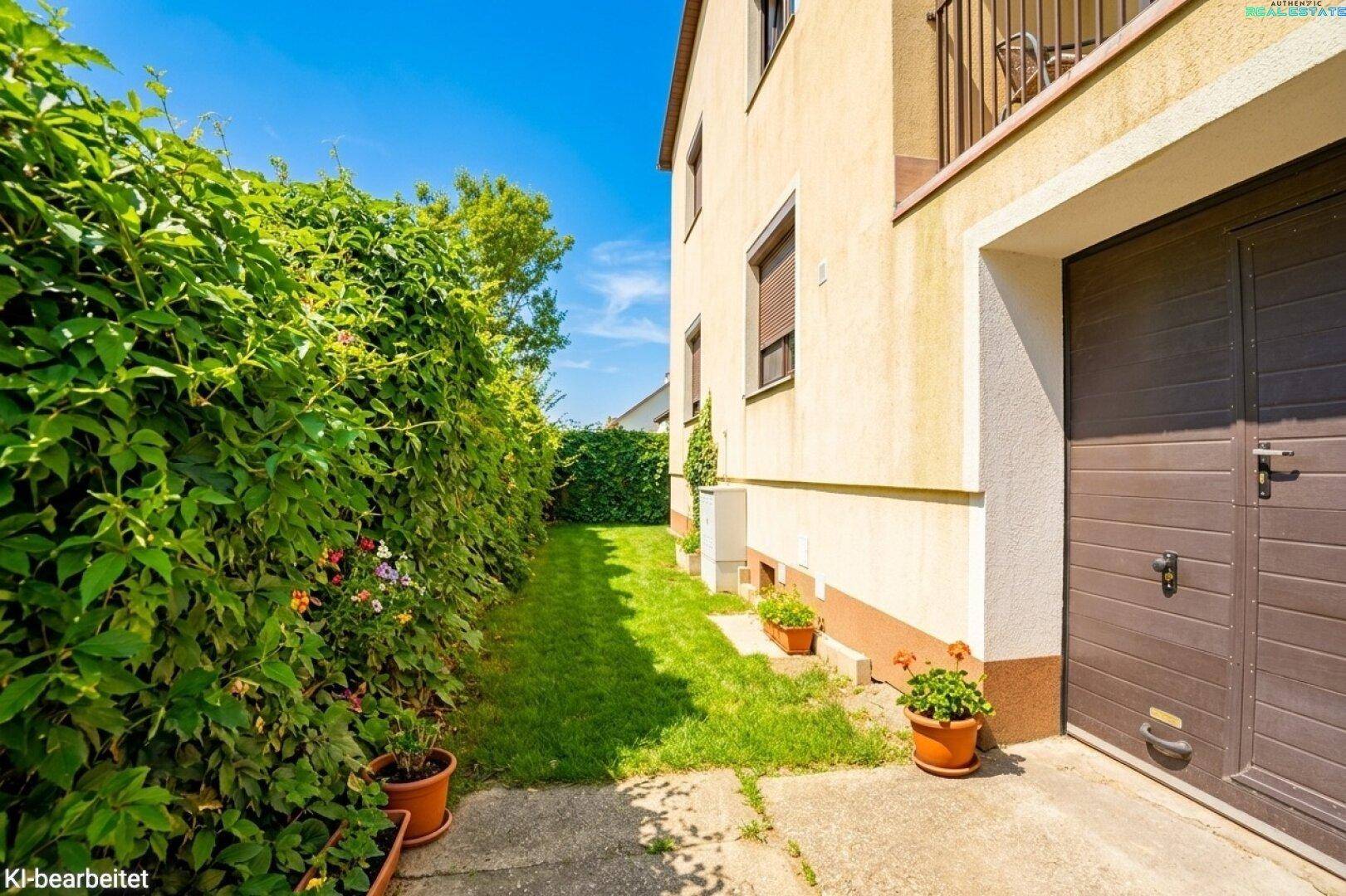 Seitenansicht des Hauses mit grünem Weg, hoher Hecke und Garagentor.