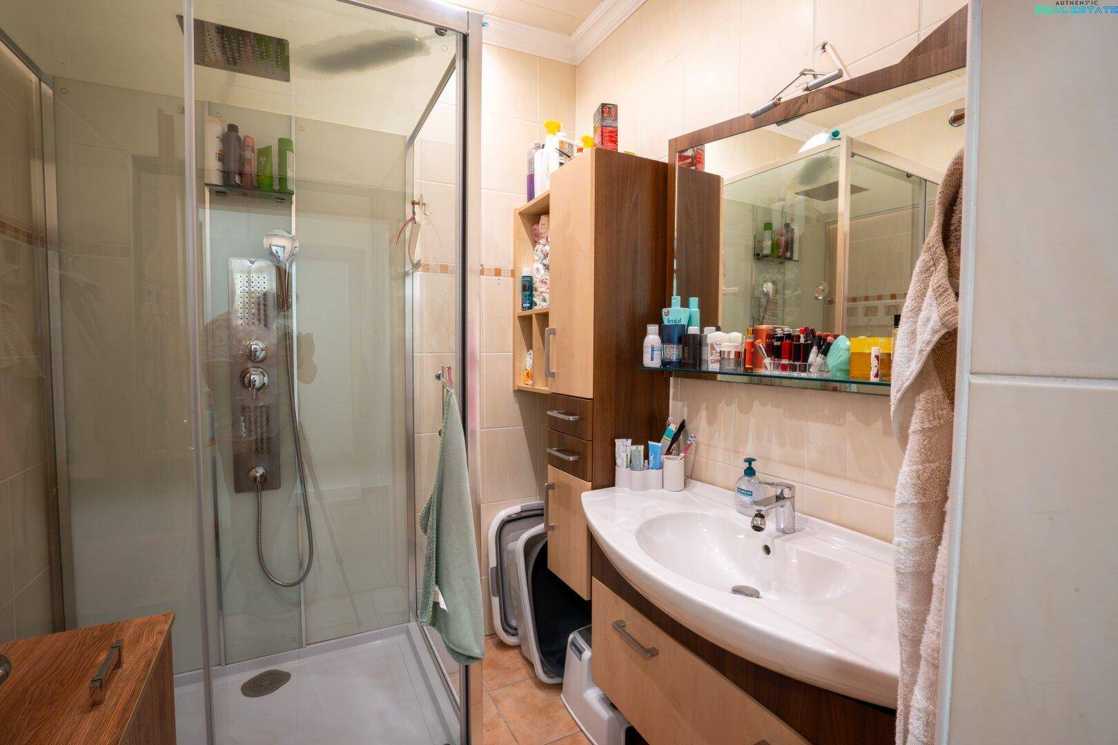 Praktisches Badezimmer mit Duschkabine, Einzelwaschbecken und Spiegelschrank, hell gefliest.