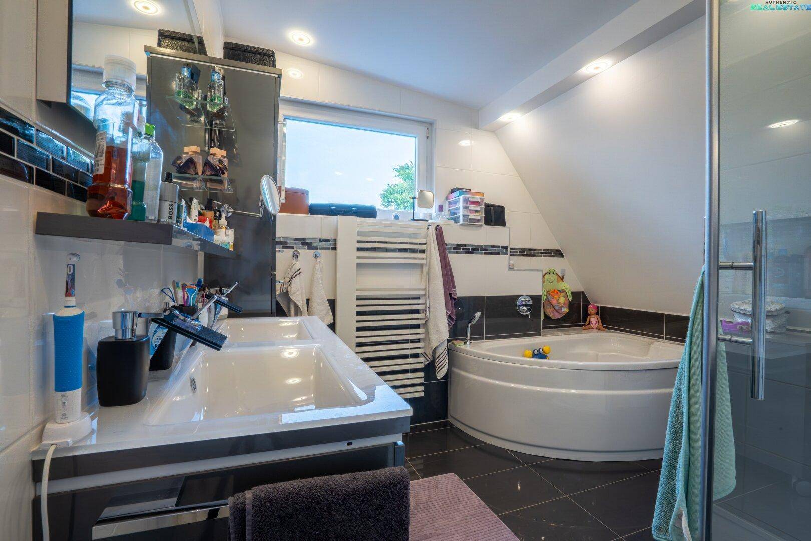 Helles Badezimmer mit Eckbadewanne, Doppelwaschbecken und Dachschräge, modern gefliest.