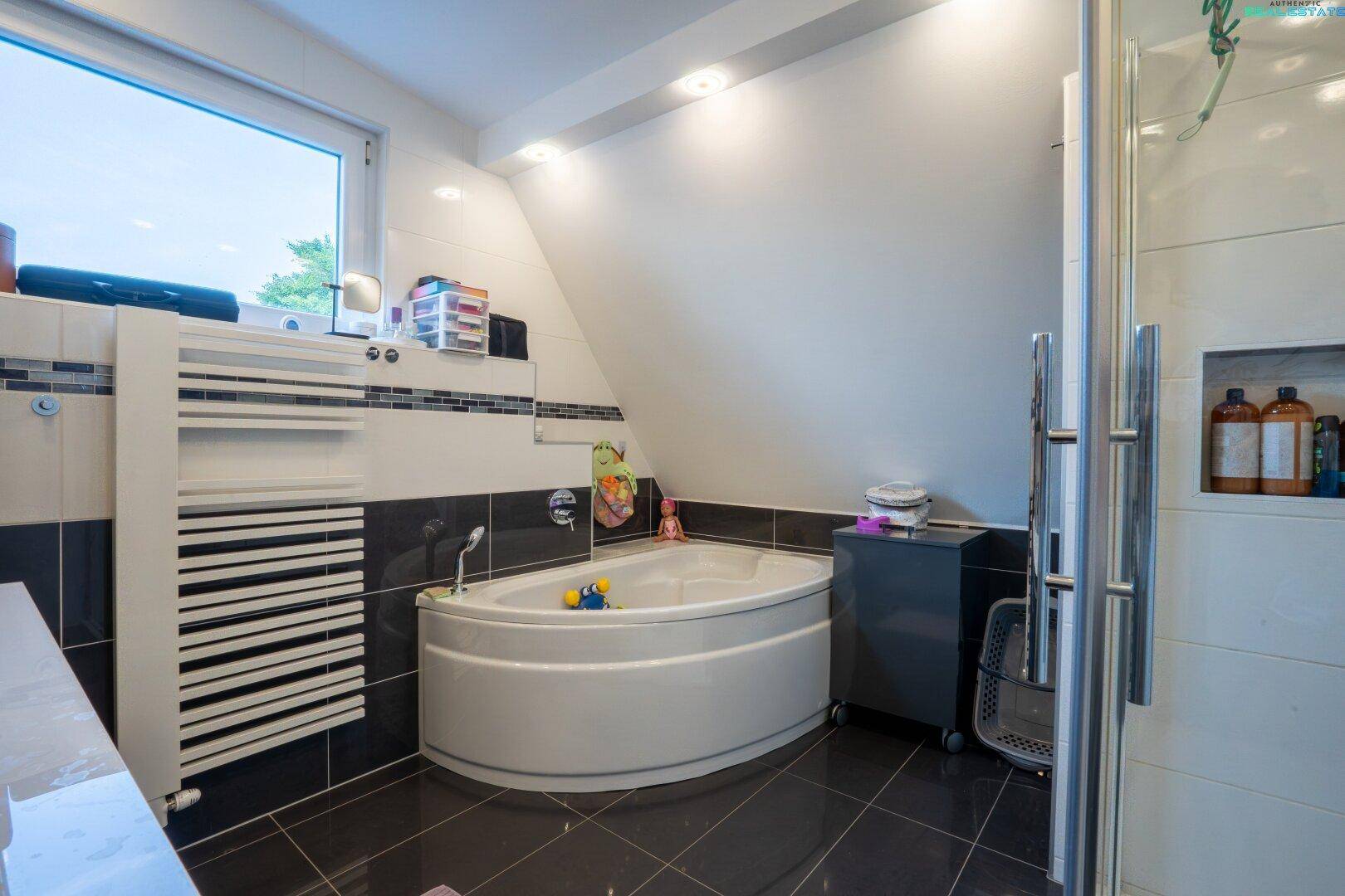 Geräumiges Badezimmer mit Eckbadewanne, beheiztem Handtuchhalter und Fenster unter Dachschräge.
