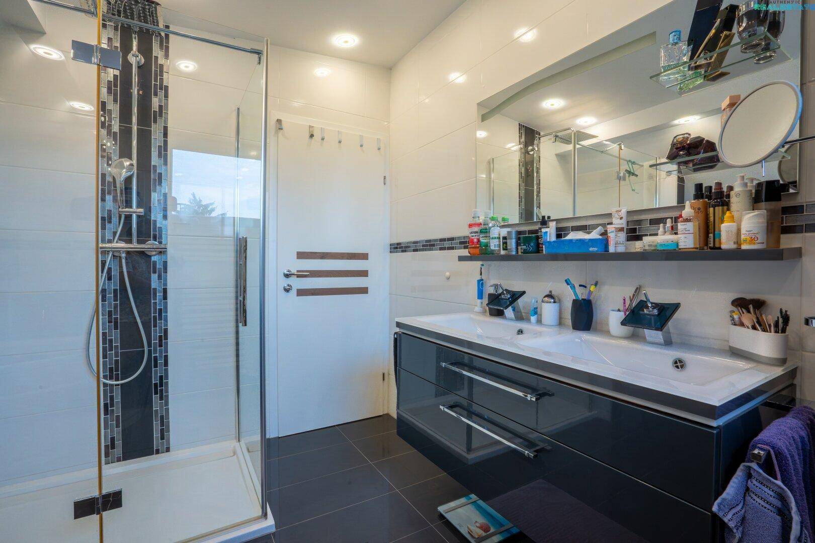 Modernes Badezimmer mit großer Duschkabine, Doppelwaschbecken und großem Spiegel.