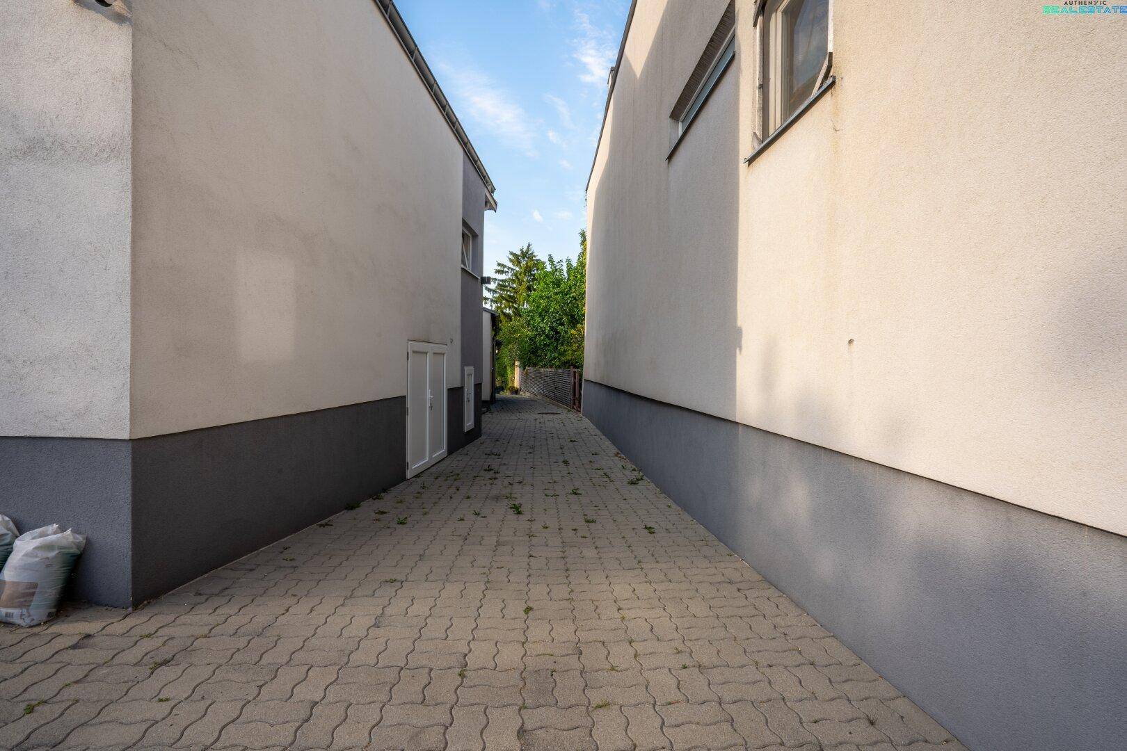 Schmaler gepflasterter Weg zwischen zwei Gebäuden mit schlichten Fassaden.