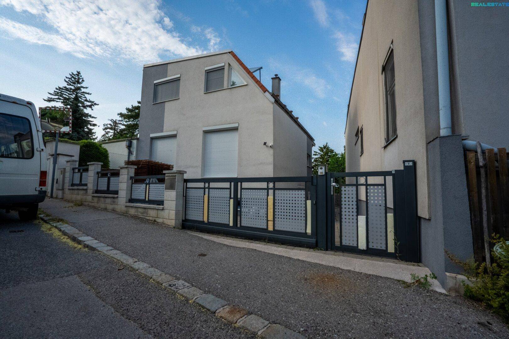 Ansicht der modernen Hausfassade mit Einfahrtstor und angrenzender Straße.