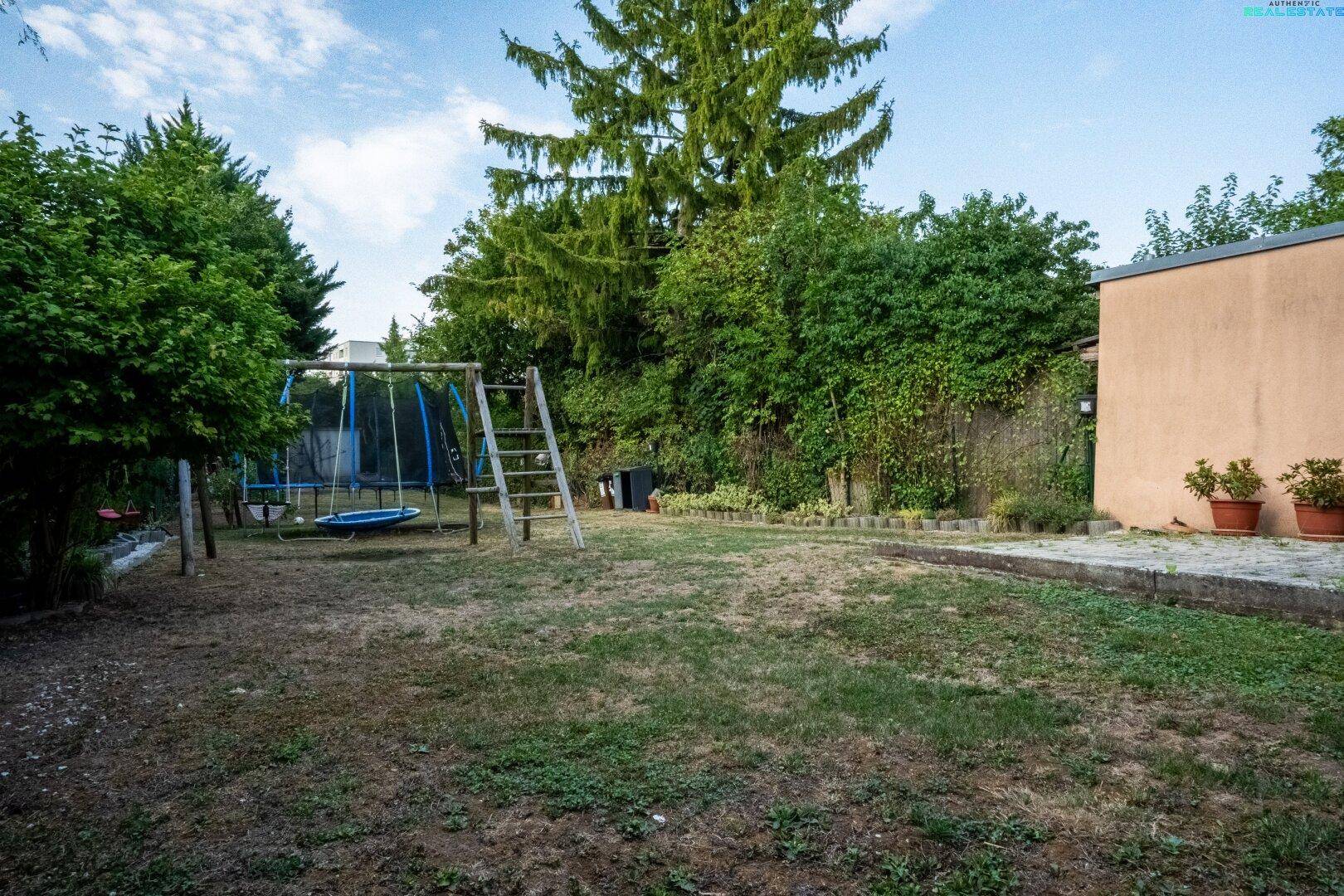 Weitläufiger Garten mit Rasenfläche, Schaukel und Trampolin für Kinder.