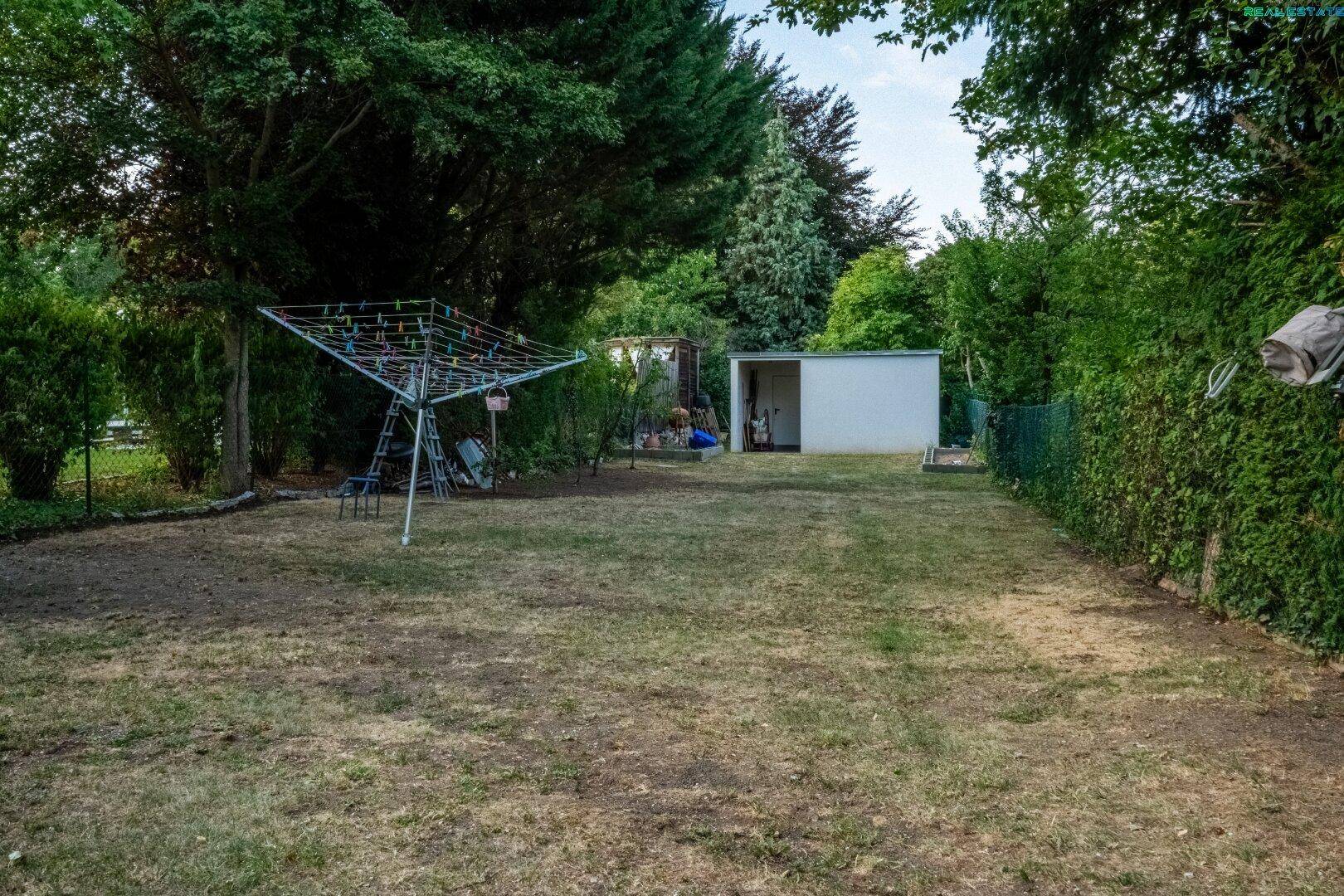 Großer Rasenbereich im Garten mit Wäschespinne und einem Gartenhaus im Hintergrund.