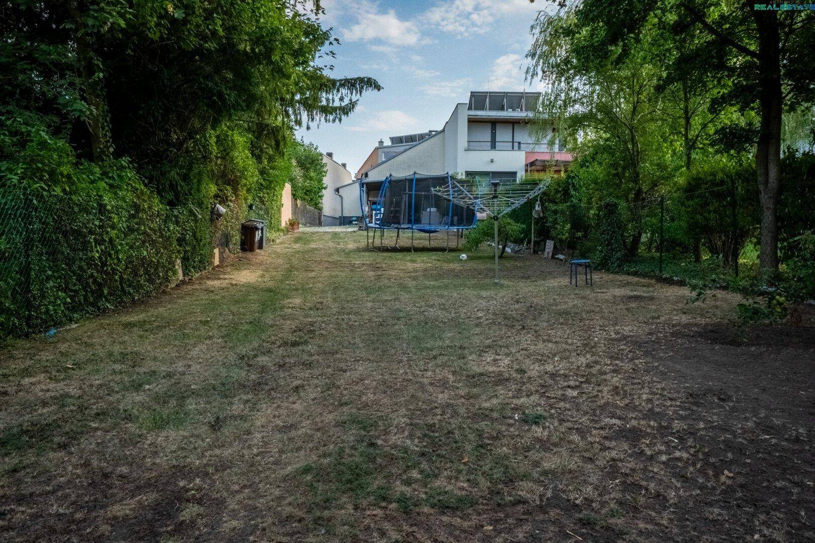 Großer Rasenbereich im Garten mit Trampolin und Blick auf das Hauptgebäude.