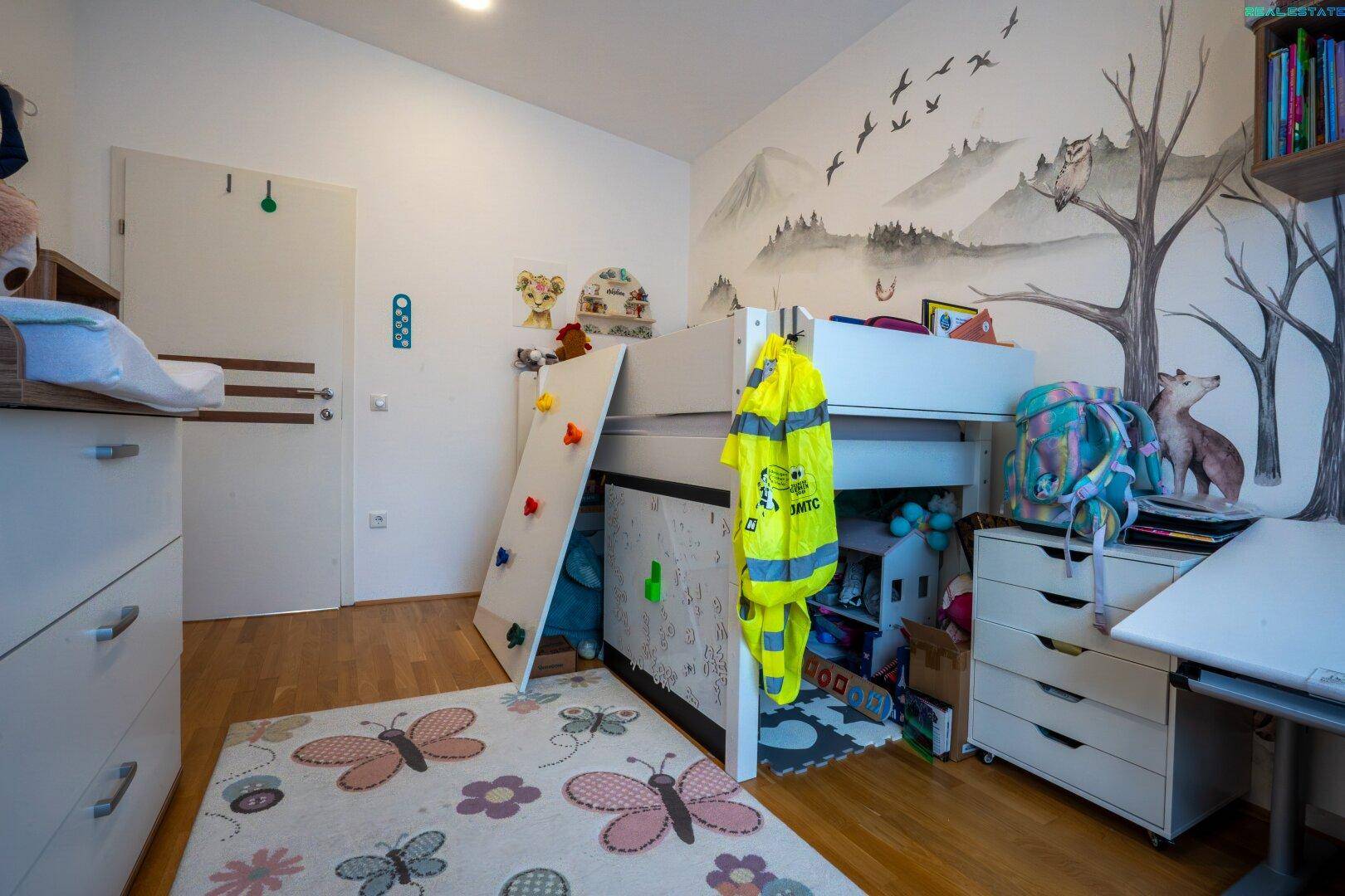 Kinderzimmer mit Hochbett, Schreibtisch und verspielter Wandgestaltung.