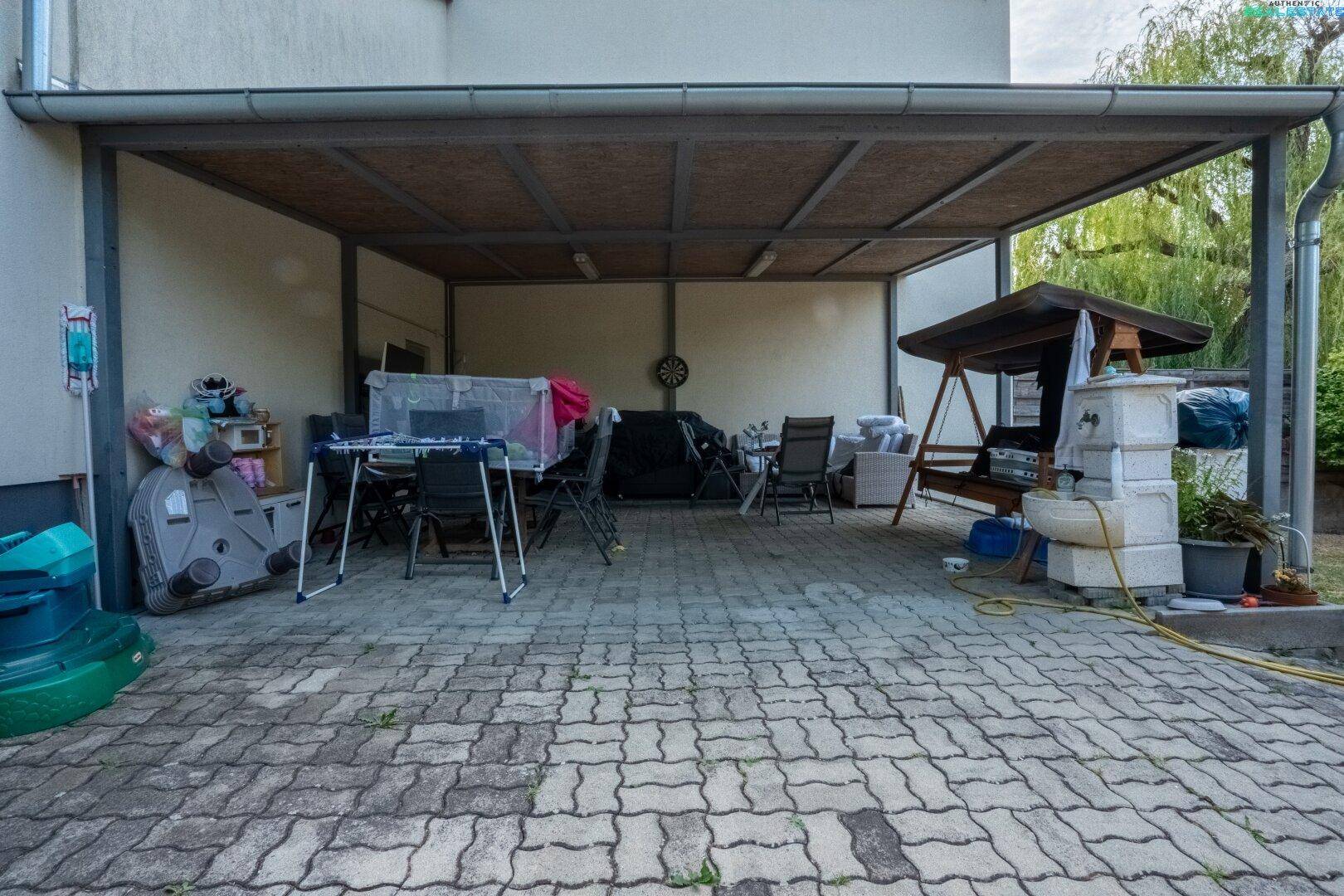 Überdachter Carport-Bereich mit gepflastertem Boden und Abstellmöglichkeiten.
