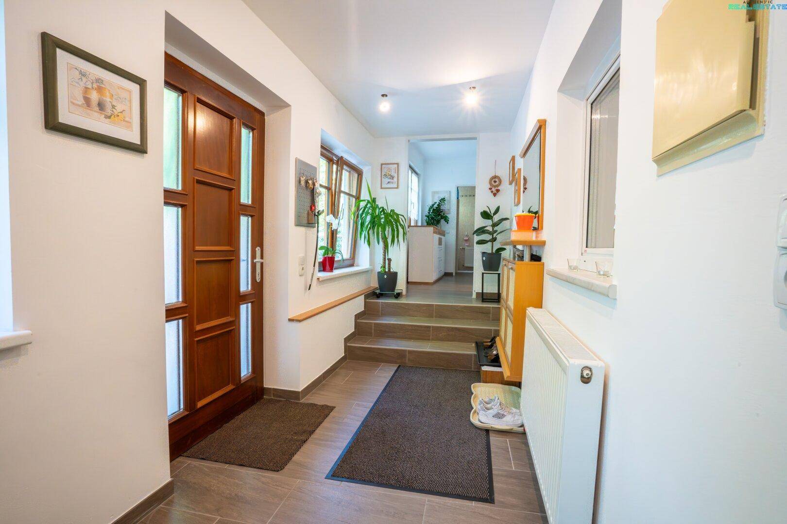 Heller Eingangsbereich mit Holztür, gefliestem Boden und Treppe zum oberen Stockwerk.