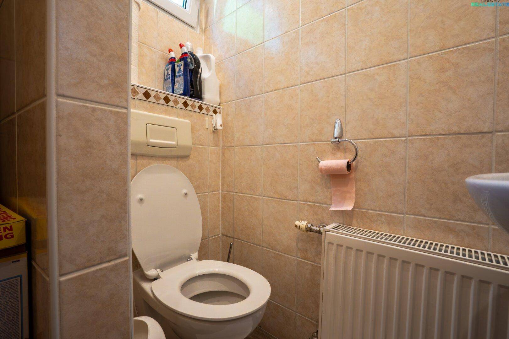 Kleines Gäste-WC mit WC, Waschbecken und Heizkörper, komplett gefliest in Beige.