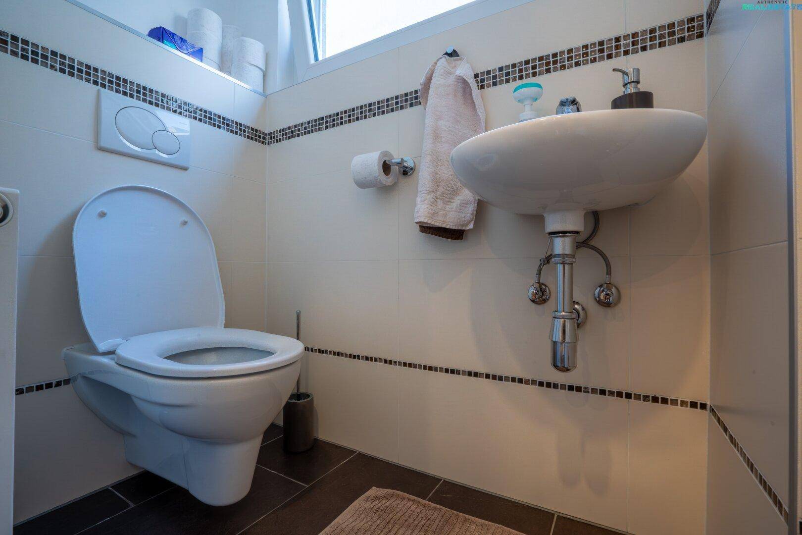 Kleines Gäste-WC mit Wand-WC, Waschbecken und Fenster, modern gefliest in Weiß und Schwarz.