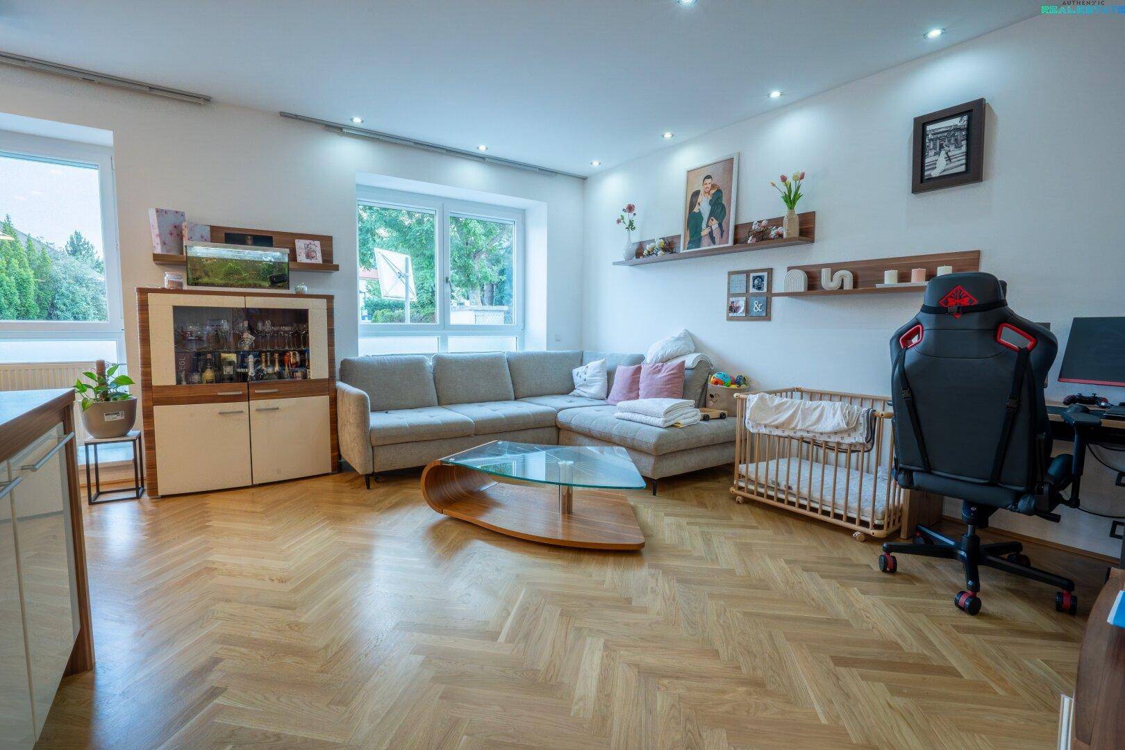 Gemütliches Wohnzimmer mit großem Sofa, Parkettboden und Babybett.