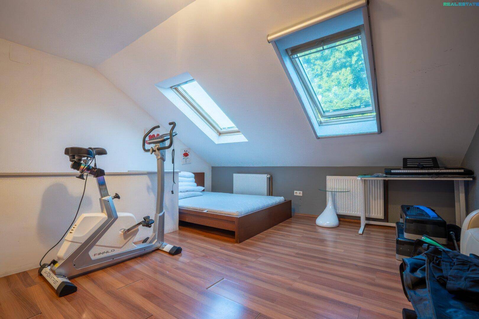 Dachgeschosszimmer mit Dachschrägen, Dachfenstern und Sportgerät, vielseitig nutzbar.