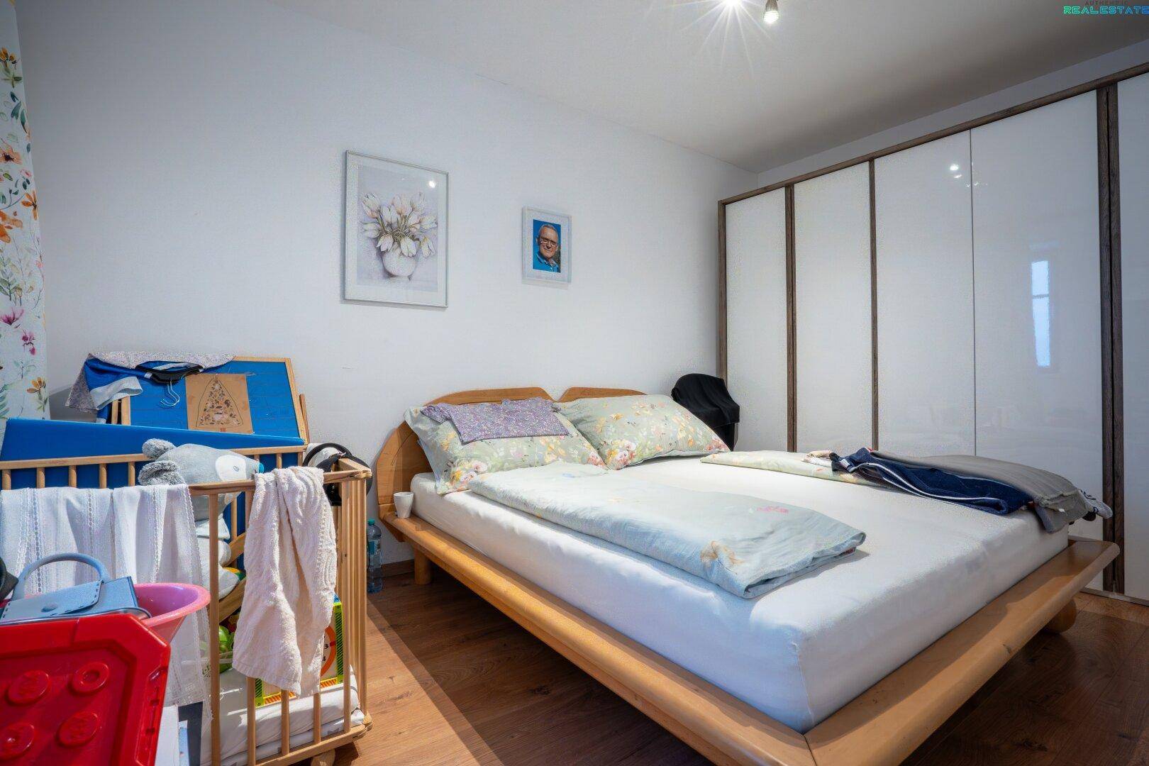 Helles Schlafzimmer mit Doppelbett, weißen Einbauschränken und Babybett.