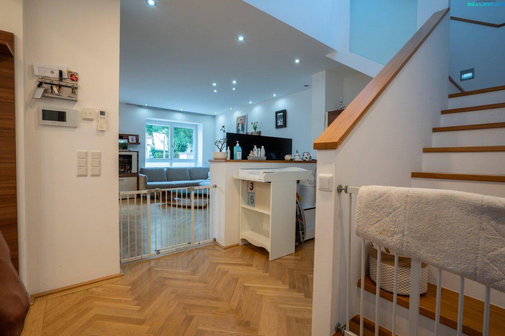 Heller Flur mit Holztreppe, Parkettboden und Zugang zum offenen Wohnbereich.