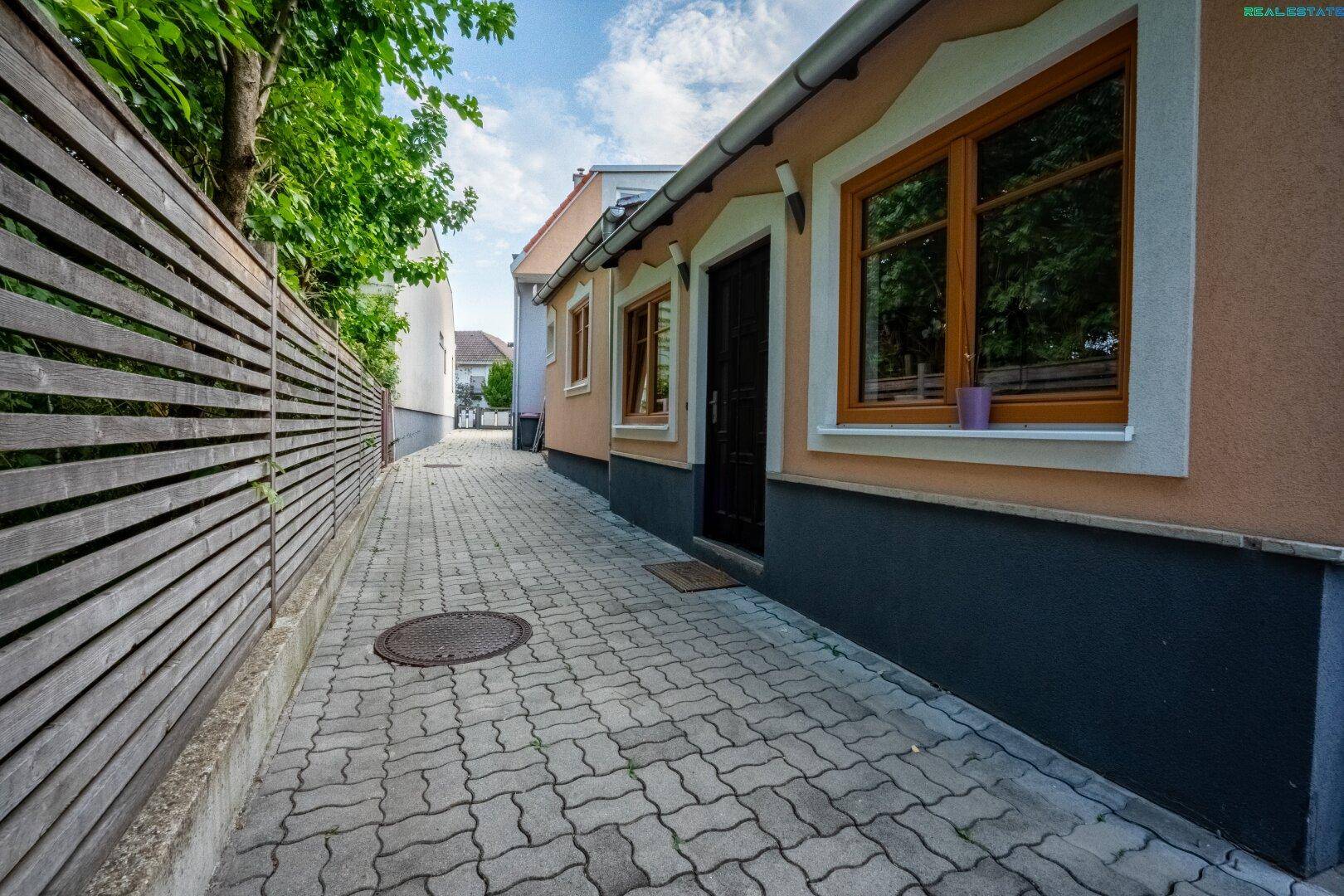 Gepflasterter Zugangsweg zum Haus mit Holzzaun und grüner Bepflanzung.