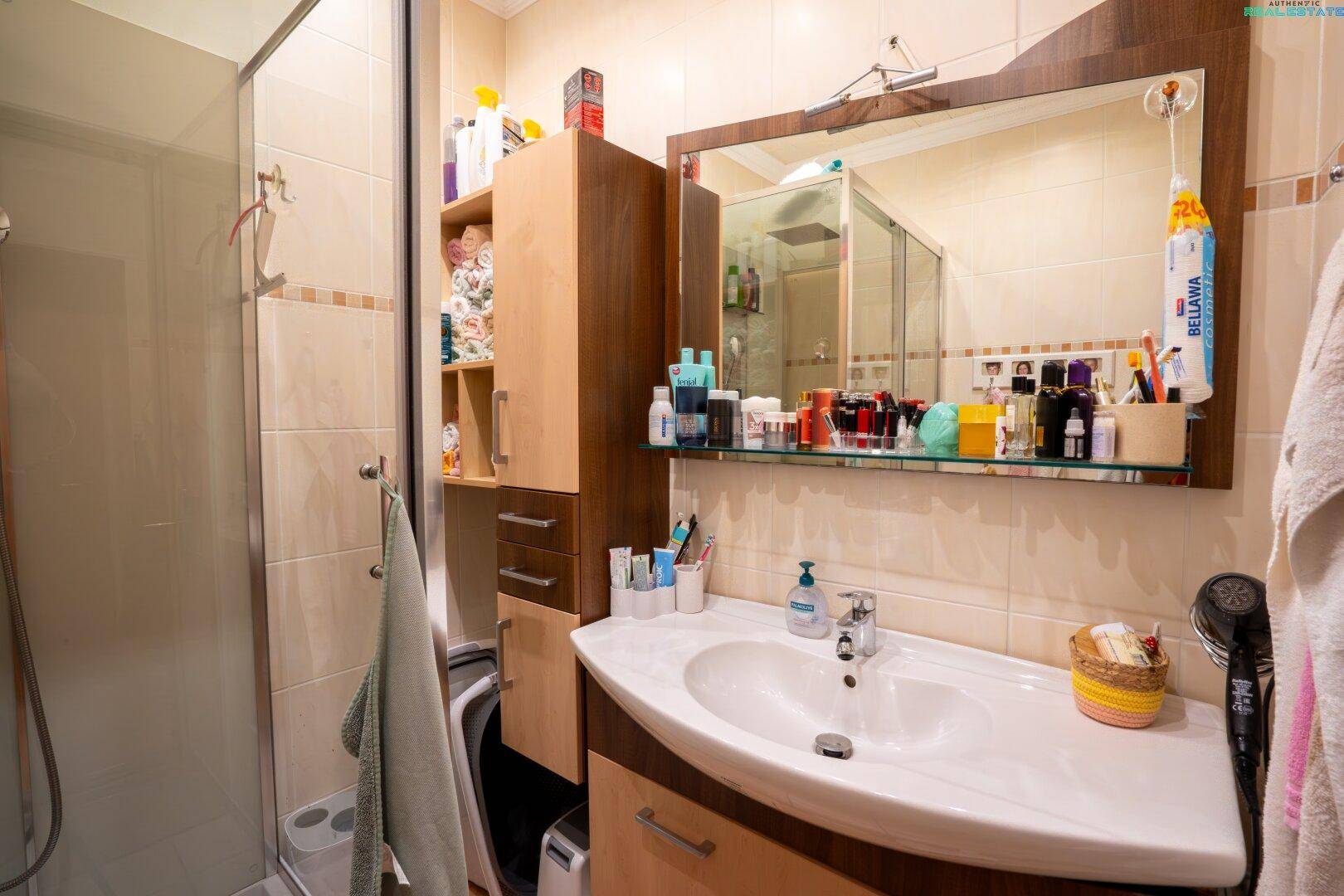 Funktionelles Badezimmer mit Duschkabine, Einzelwaschbecken und Spiegelschrank, in warmen Farbtönen.