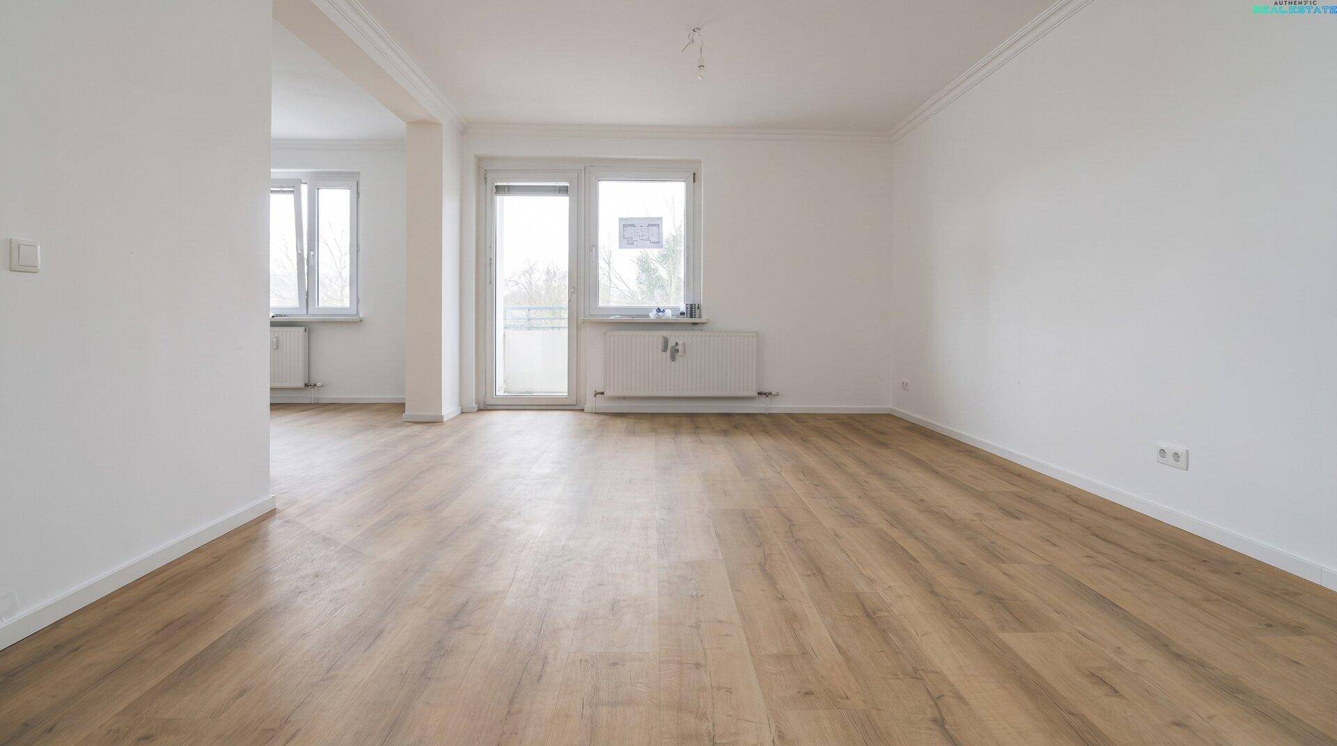 Geräumiger, heller Raum mit Holzboden und Zugang zu einem Balkon oder einer Terrasse.